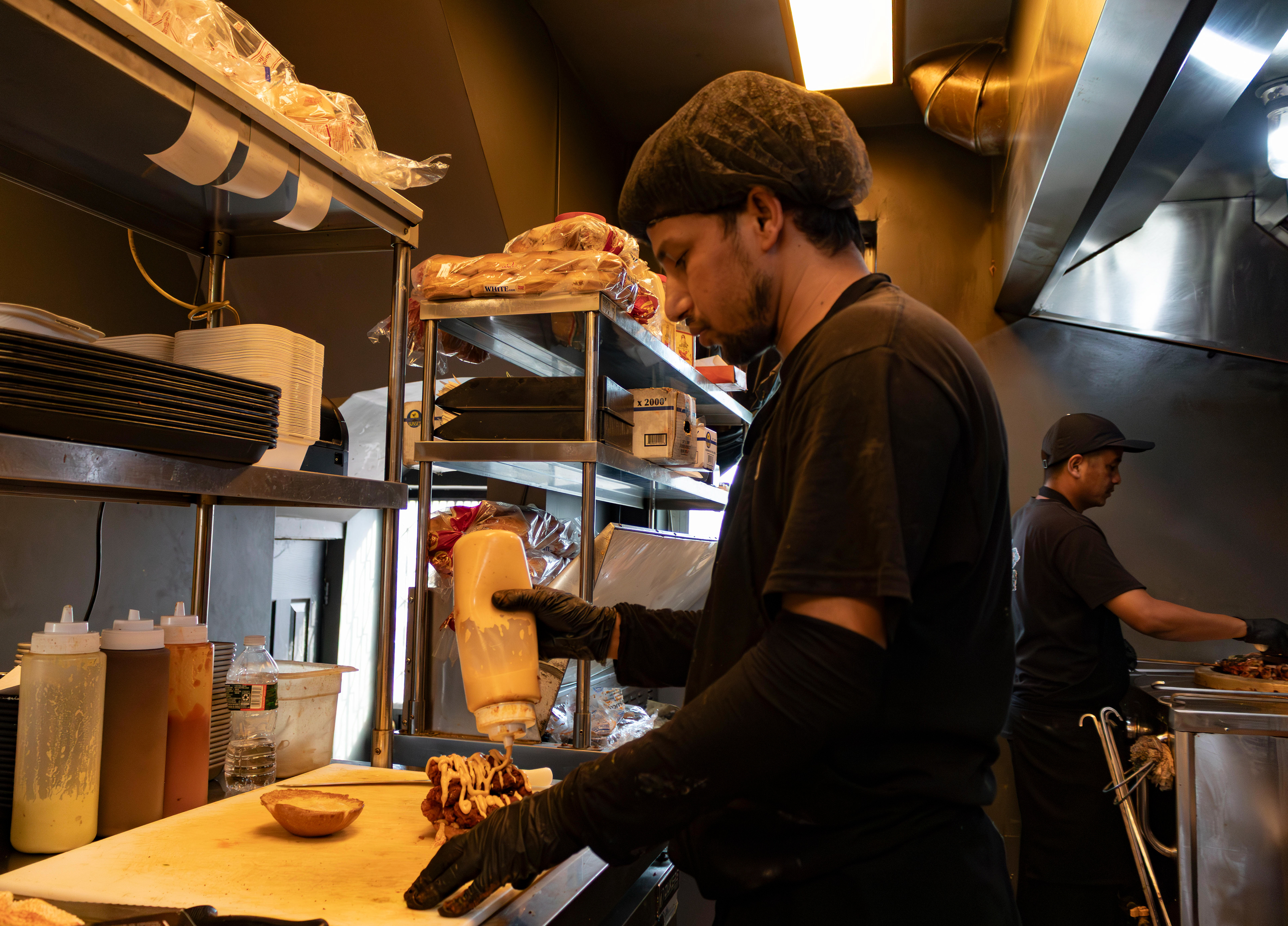 One cook (left) prepares a fried chicken sandwich while the other cook (right) slices up another skewer of chiken tikka cubes with a chef's knife. Photo by Sunah Choudhry.