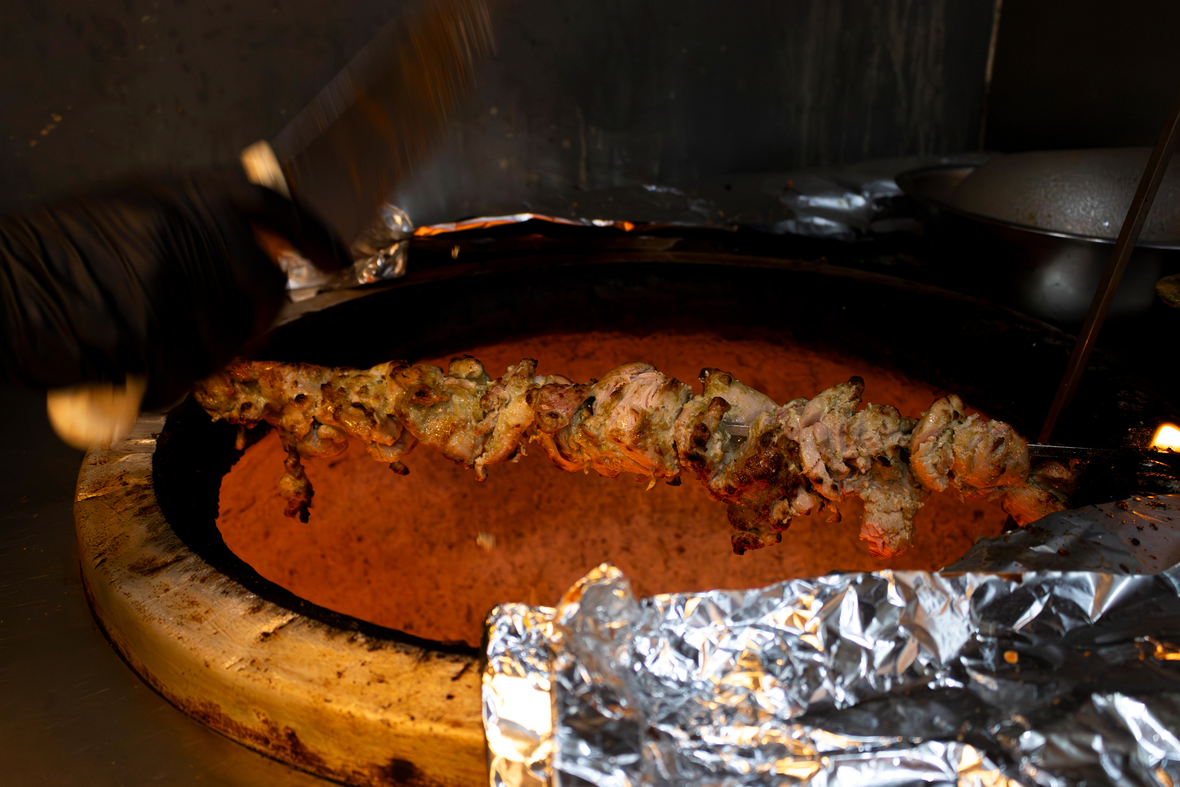 One of the cooks uses a chef's knife to slice the chicken over the tandoor. Photo by Sunah Choudhry.