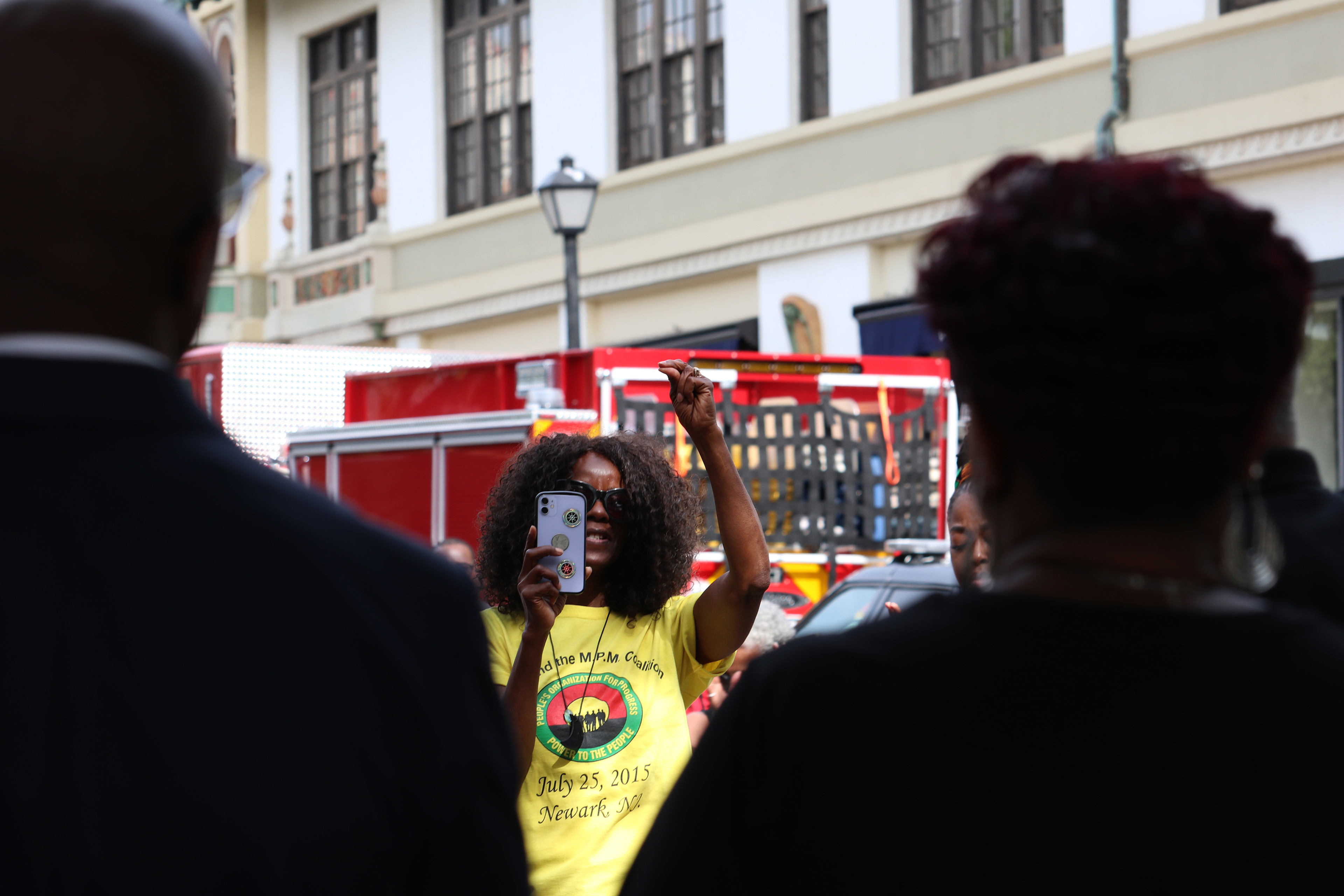 MONTCLAIR, NJ 06/19/2026 JUNETEENTH FLAG RAISING: People’s Organization For Progress’ social media ambassador, Susan Saintweather, records and cheers on Founder Larry Hamm at Montclair’s Juneteenth flag-raising ceremony on the corner of Church Street and Bloomfield Ave. Montclair residents gather to honor and celebrate Juneteenth, listen to local politicians and leaders, and watch a performance by the students from Beyond the Boogie Dance Company. Photo by Sunah Choudhry.