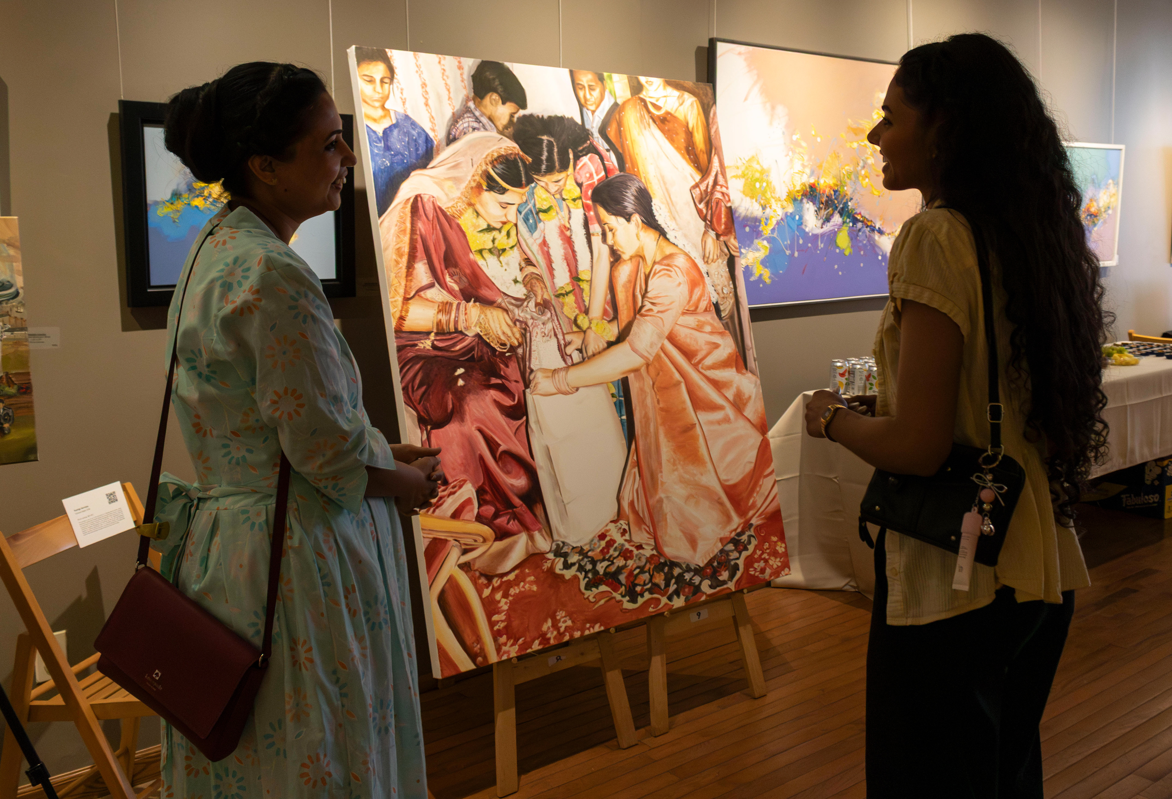NEW BRUNSWICK, NJ 06/20/2026 CANVAS AND KAHANI: Resin artist Pranali Bharambe and Artist and Rutgers alumna Rushiga Sarveiya discuss her oil painting named “Sudama Nagar.” Central Desi, a South Asian news publication, hosts its first-ever art showcase and open-mic at Alfa Art Gallery on Church Street. Photo by Sunah Choudhry.