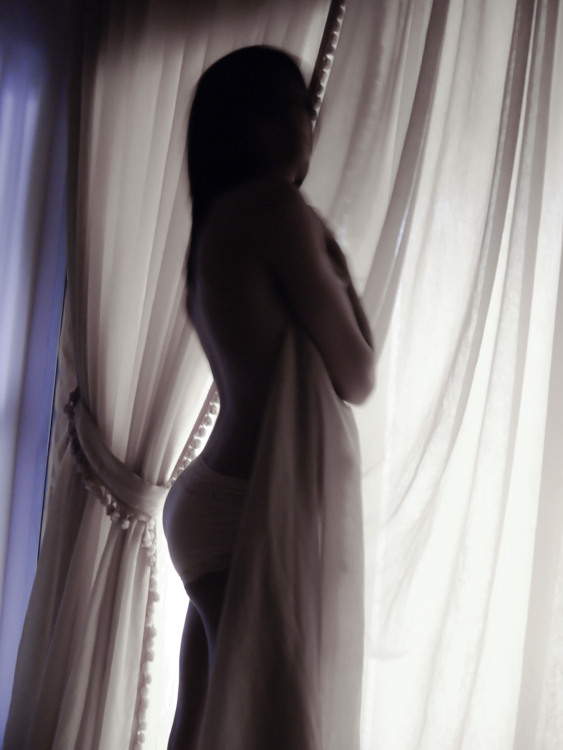 Femme en transparence entre la lumière et un voilage