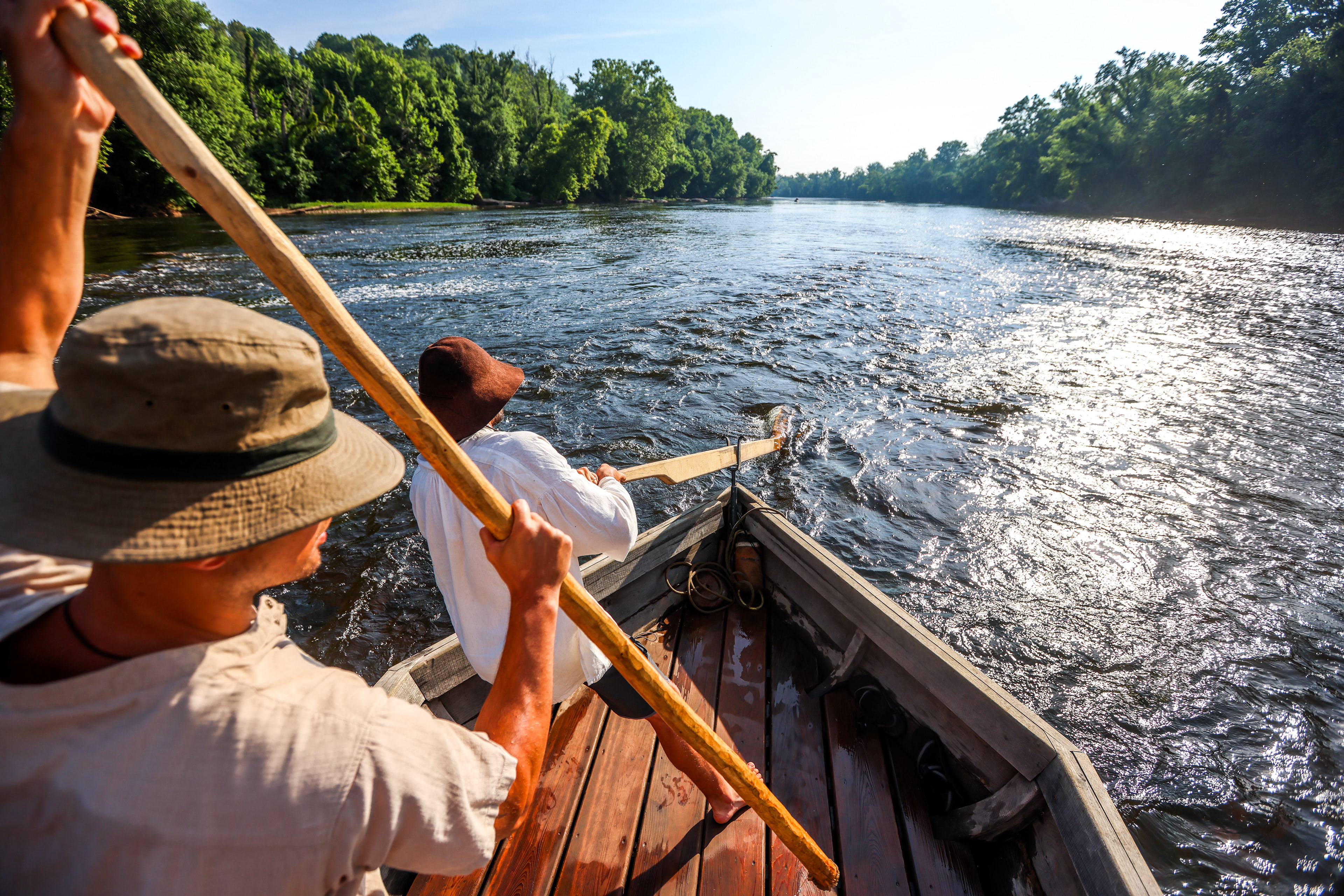 Will Cash, left, and Will Smith, right, drive their batteau, the Morning Dew, down the James River on Wednesday, June 19, 2024, on their way to Scottsville. Cash uses a wooden pole to propel the boat, while Smith wields the sweep oar, which turns the boat left or right.
