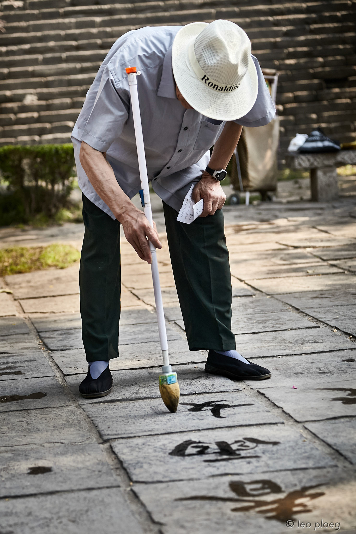 Man painting Mandarin characters in water on brick stones in a park