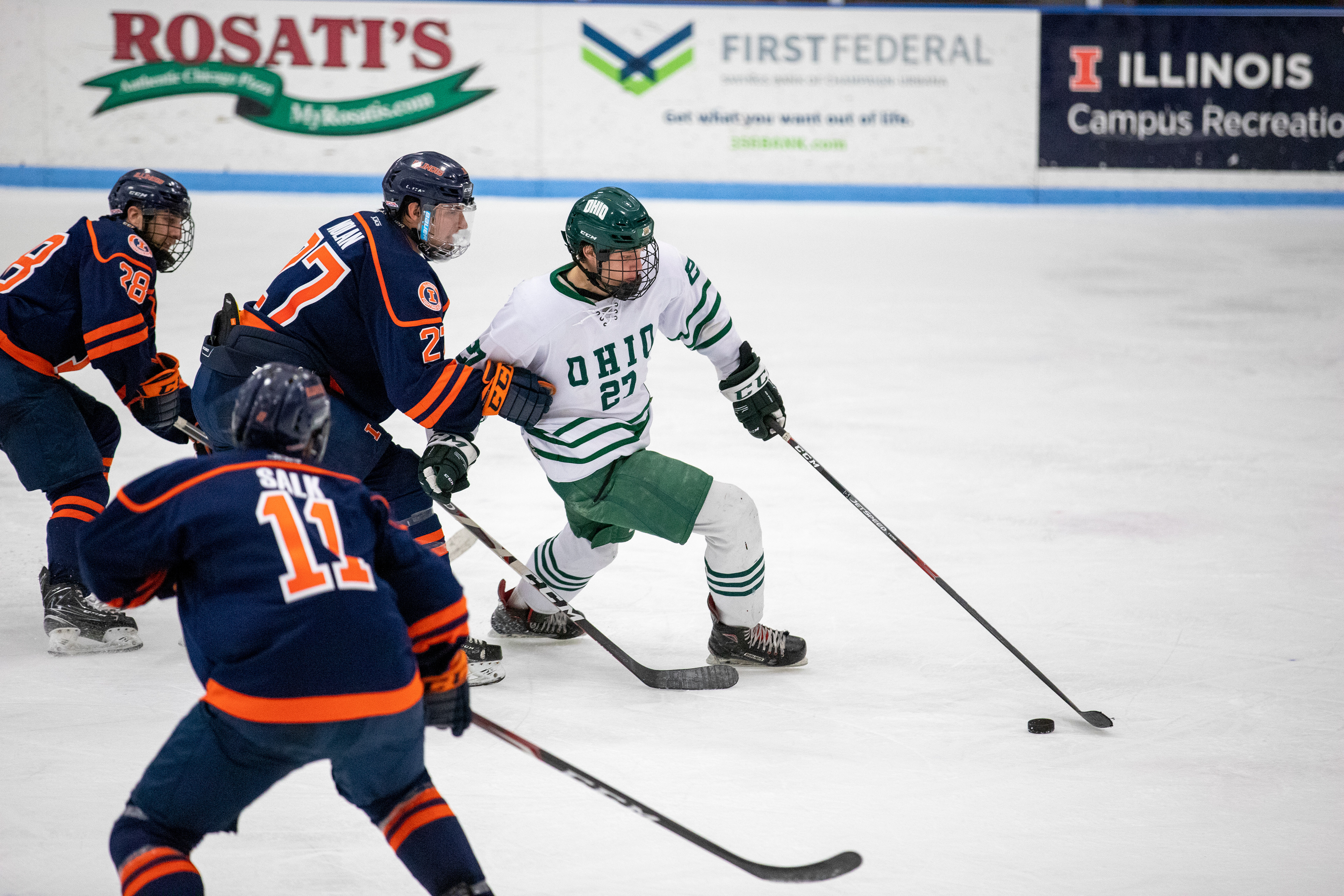 Sam Turner (#27, white) breaks in towards the net, while being pursued and held by Illini defenders.