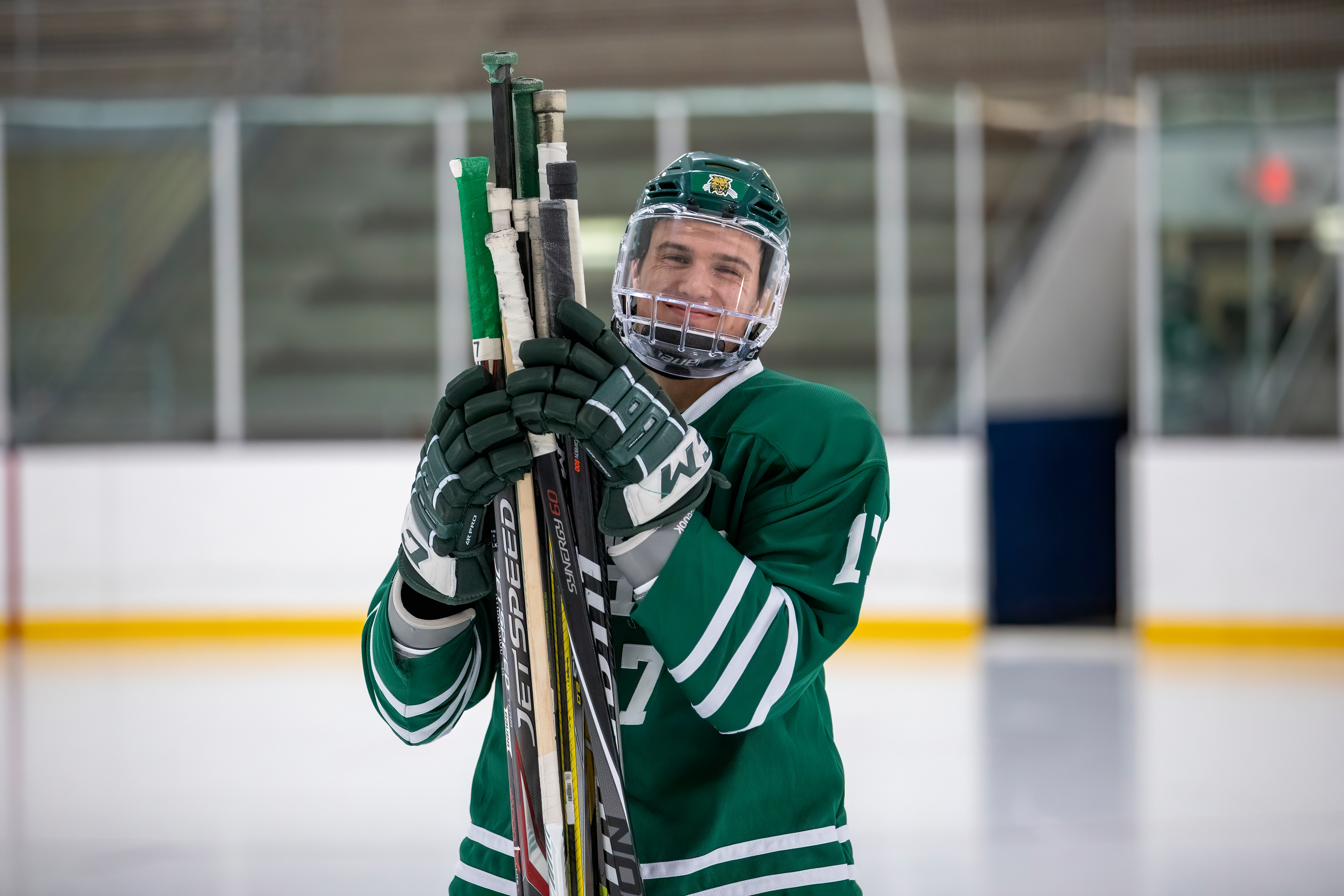 Blake Rossi smiles for the camera as he carries sticks out onto the ice.