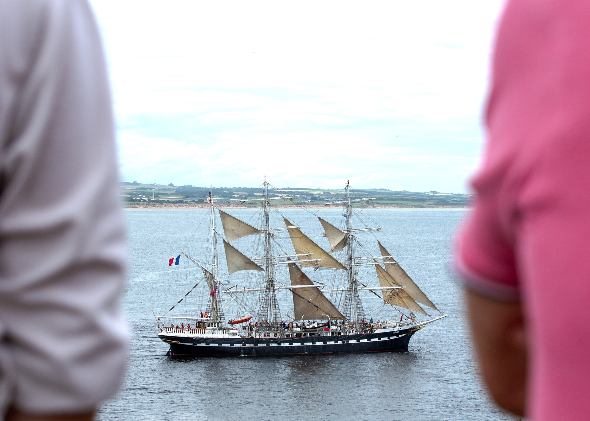 Framed by two onlookers, the Dutch ship slips out of Aberdeen—an in-between moment where curiosity meets departure, and the North Sea opens the way to Norway