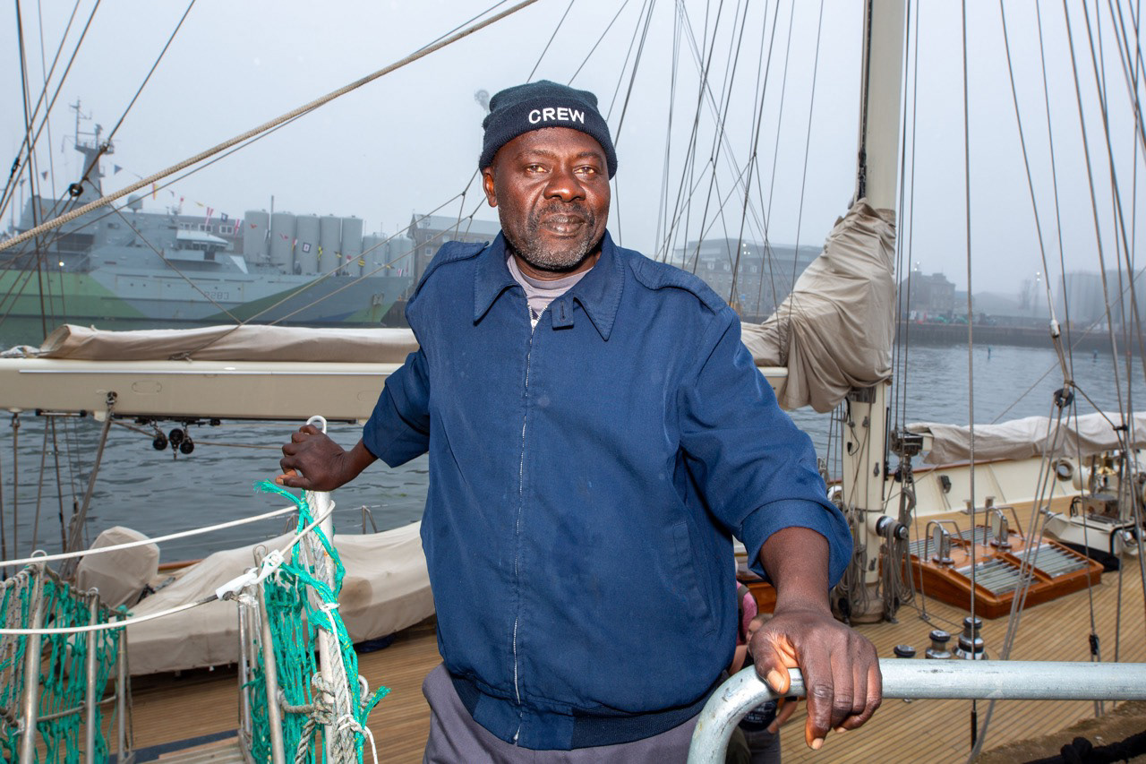 A quiet pause between duties, a crew member stands still for a moment, framed by rope, salt air, and the rhythm of the harbour