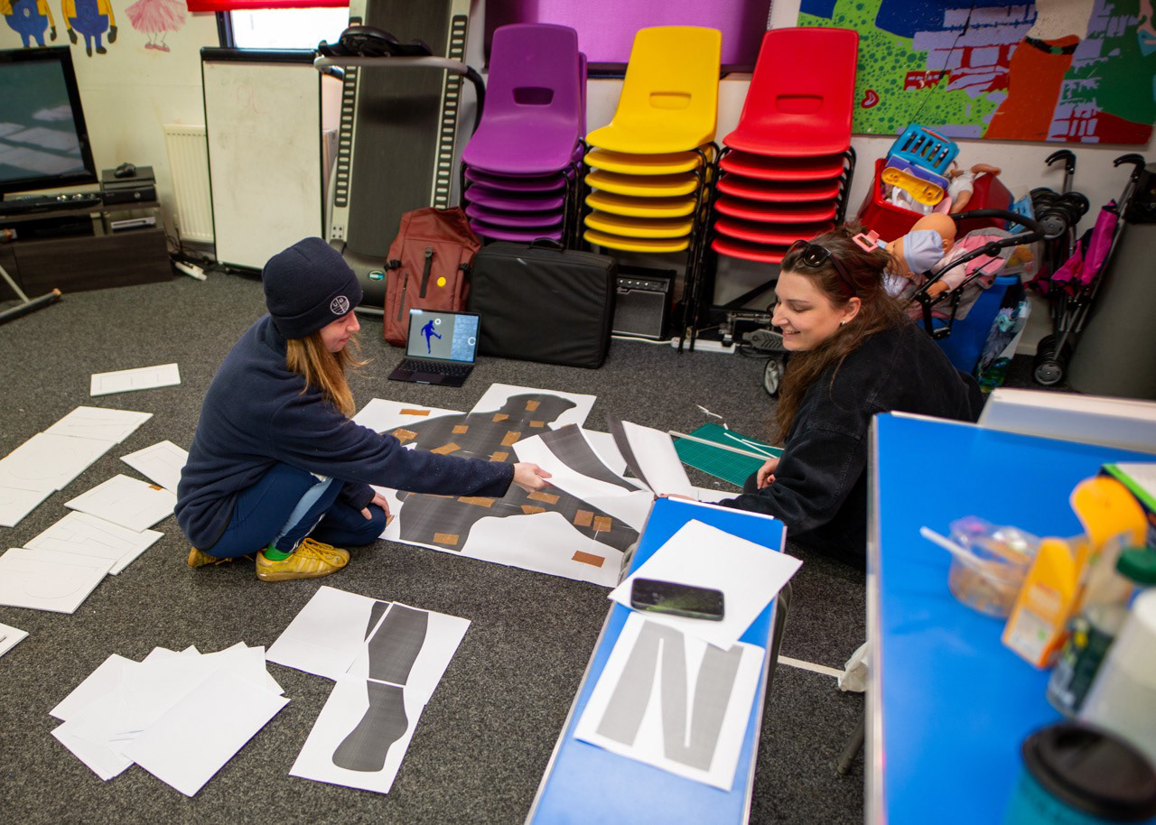 Nina and Maddie carefully preparing the silhouette of Denis Law — a quiet, hands-on moment before the artwork takes shape