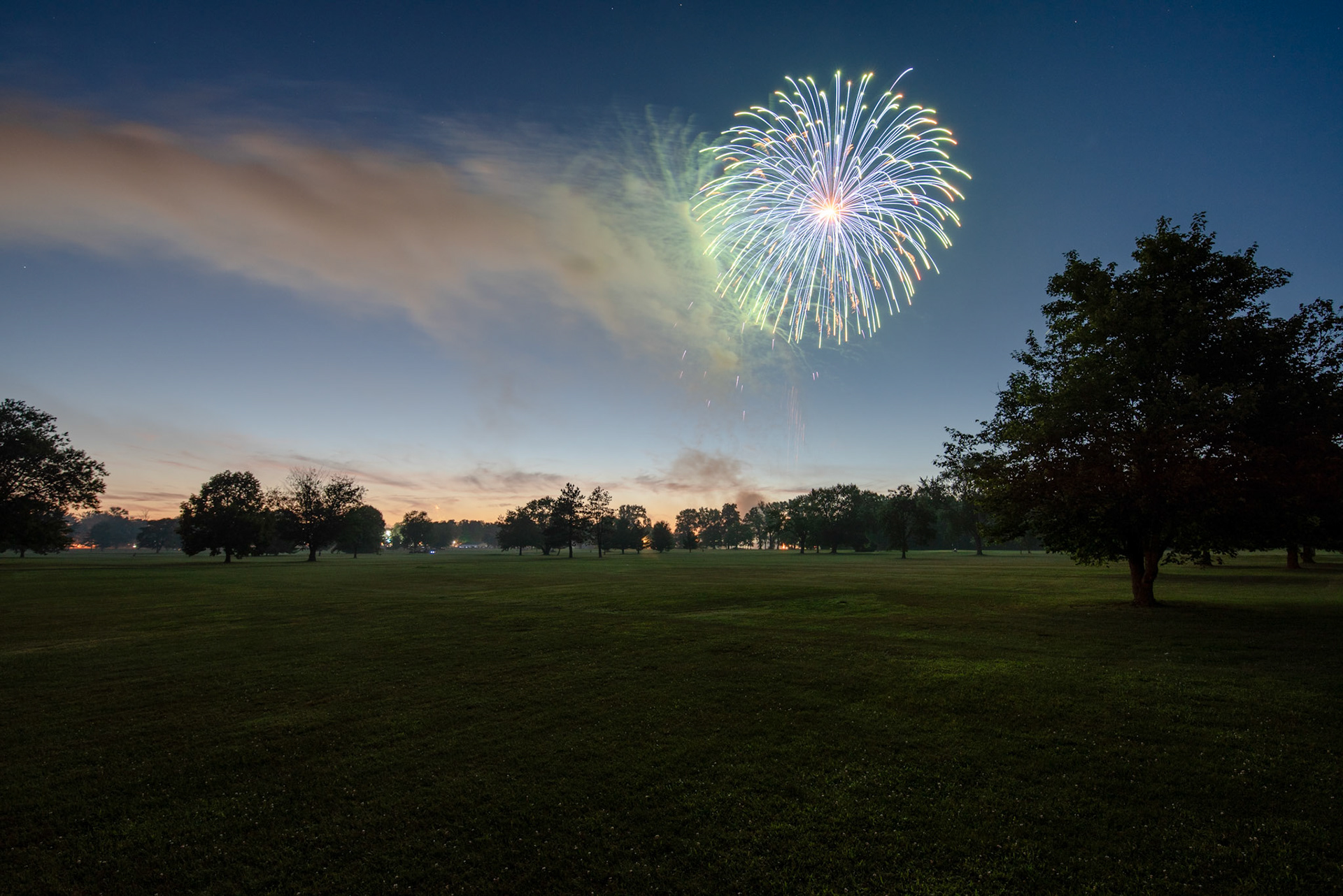 Fireworks illimunate the night sky over an open golf course.