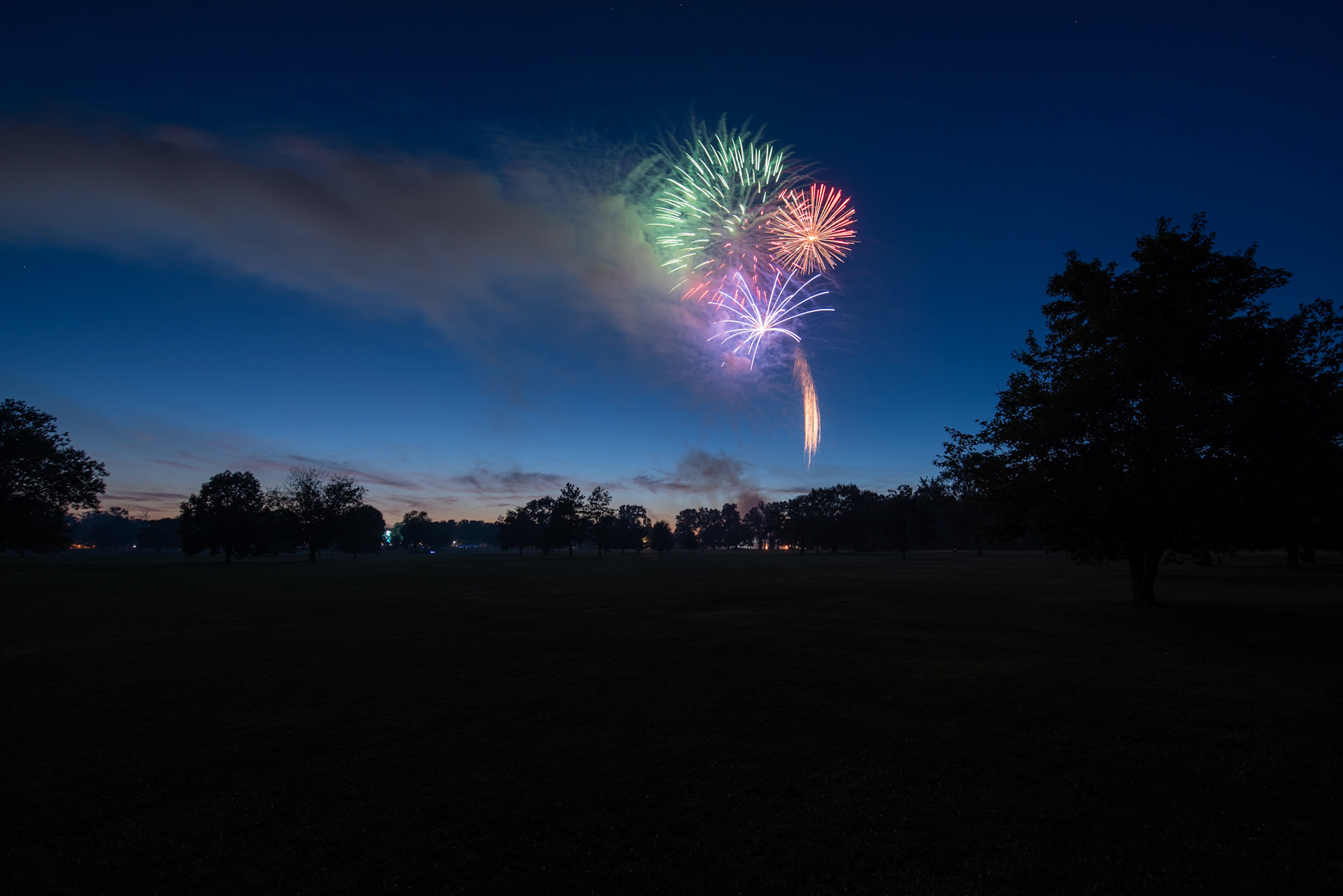 Fireworks illimunate the night sky over an open golf course.