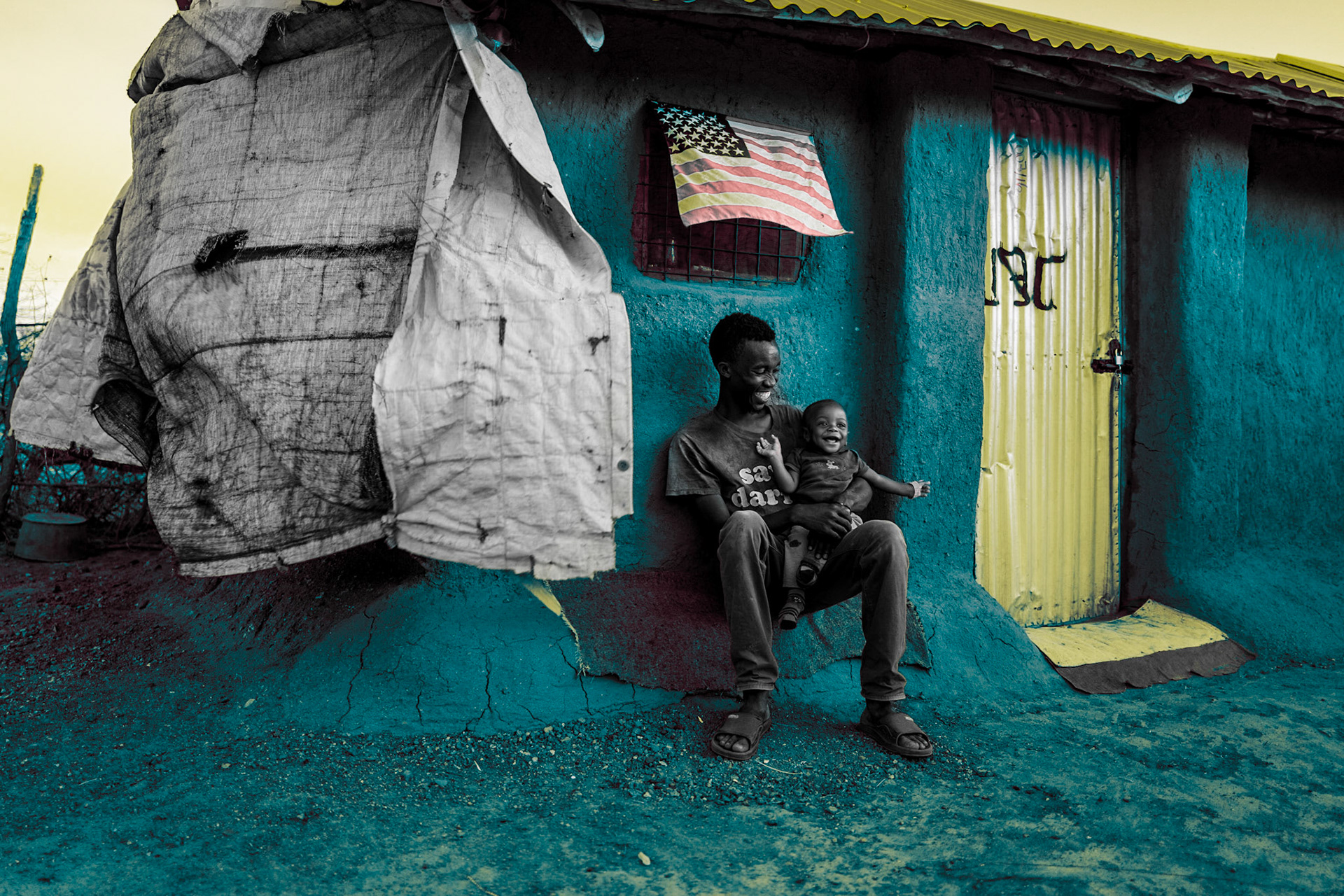 A father from the Democratic Republic of Congo sits with his baby born in a refugee camp, in front of their mud hut in Kakuma.