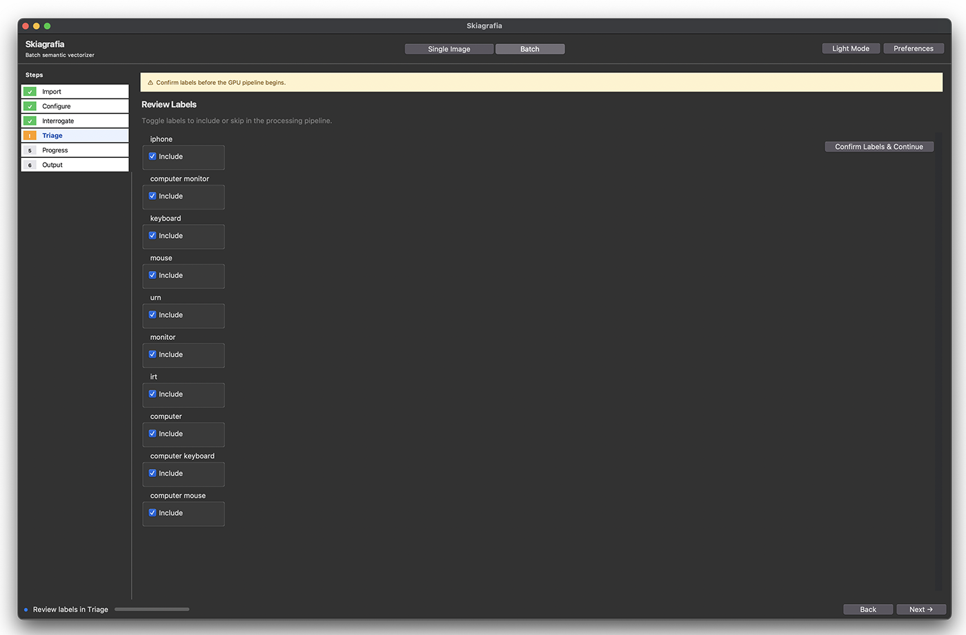 : Screenshot of Skiagrafia in Batch mode, dark theme, at the Triage step. The title bar reads "Skiagrafia / Batch semantic vectorizer". A six-step sidebar on the left shows Import, Configure, and Interrogate with green checkmarks, Triage highlighted in amber as the current step, and Progress and Output numbered but not yet reached. A yellow warning banner at the top reads "Confirm labels before the GPU pipeline begins." The main panel is headed "Review Labels" with the subtitle "Toggle labels to include or skip in the processing pipeline." Ten labels are listed vertically, each with a blue checked "Include" toggle: iphone, computer monitor, keyboard, mouse, urn, monitor, irt, computer, computer keyboard, computer mouse. A "Confirm Labels & Continue" button appears at the top right. The bottom bar shows "Review labels in Triage" with a progress indicator, and Back and Next buttons at the bottom right.