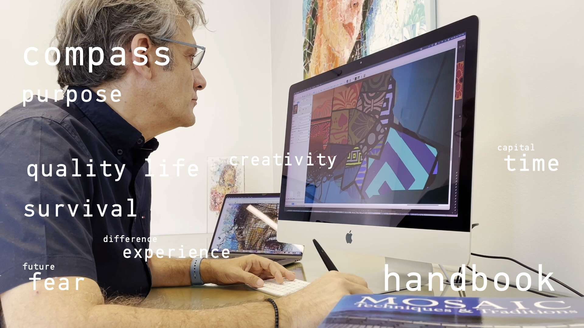 A man with graying hair and glasses, wearing a dark button-up shirt, is seated at a desk and intently focused on a large Apple iMac monitor. He is using a small white keyboard and has a stylus pen in his other hand. The computer screen displays a colorful, abstract digital artwork featuring geometric patterns in shades of purple, blue, orange, and red. On the desk, next to the keyboard, lies a book titled "MOSAIC Techniques & Traditions." In the background, other pieces of art are visible on the wall. Overlaid on the image are several words in white text, including "compass," "purpose," "quality life," "survival," "future," "fear," "difference," "experience," "creativity," "capital," "time," and "handbook," suggesting themes of work, creativity, and personal reflection.