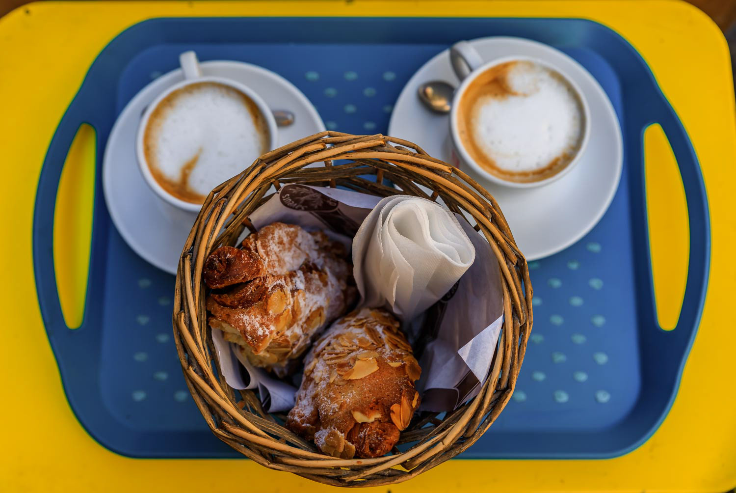 Freshly baked French almond croissants and cappuccino on a platter at breakfast at a cafe in Nice, France flat lay view 