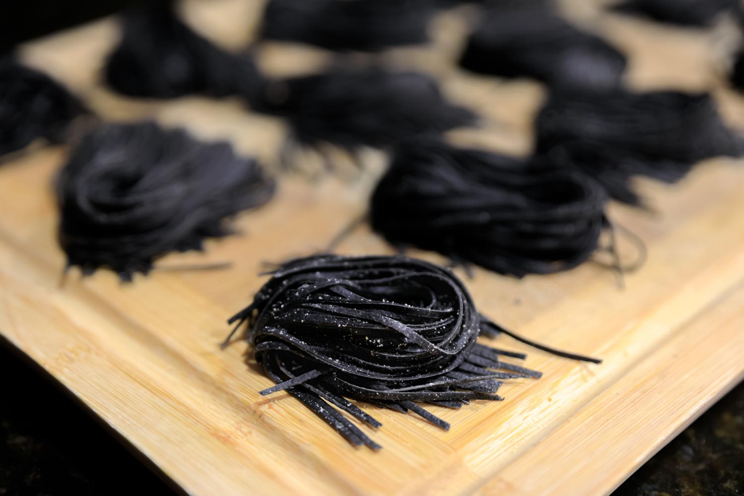 Fresh squid ink homemade spaghetti pasta nests, sprinkled with semolina flour on a wooden cutting board