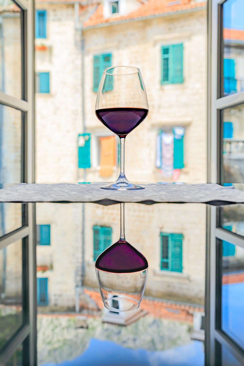 Glass or red wine with reflection and a blurred view of stone houses in old town Kotor in the background in Montenegro