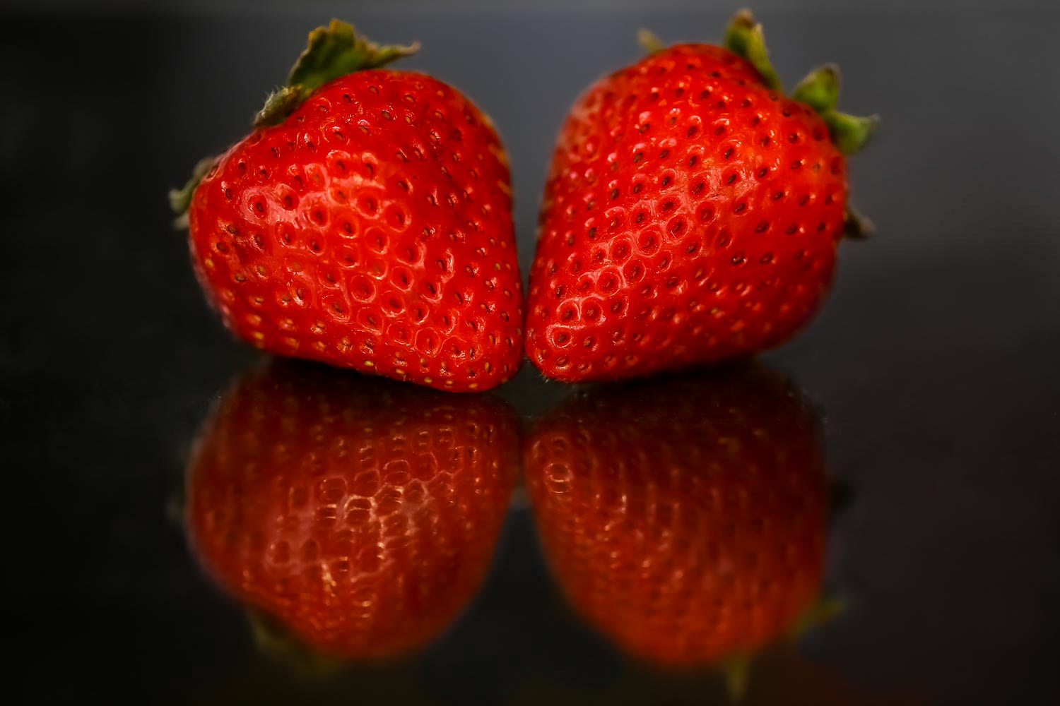 Red strawberries on black glossy background with reflection