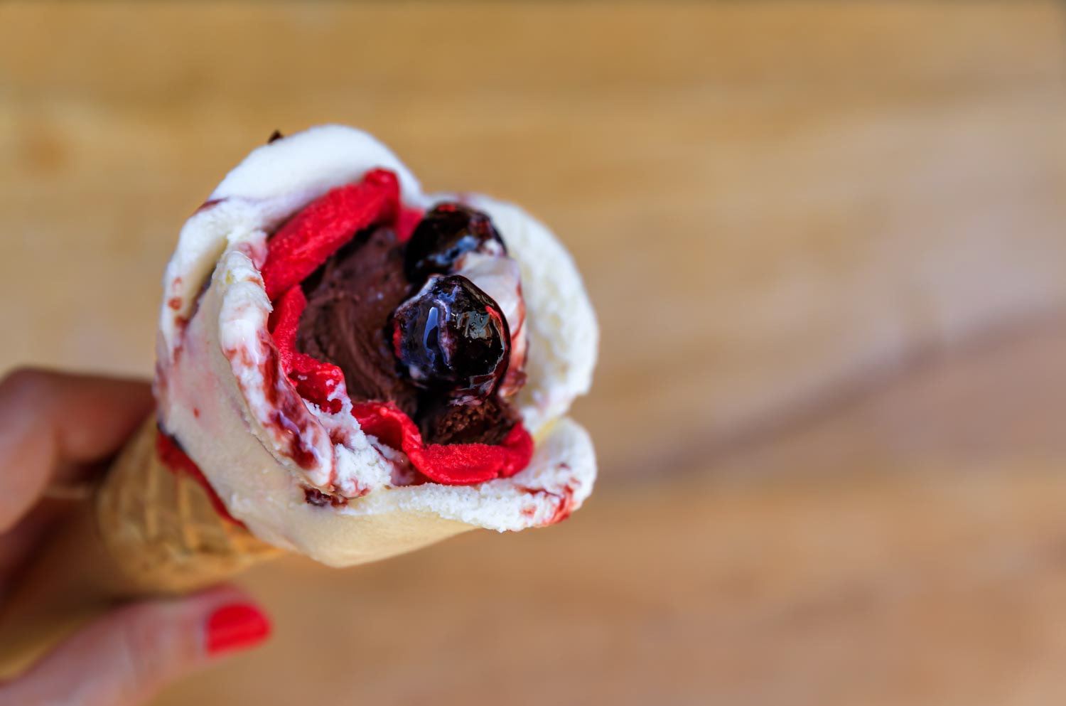 Rose shaped ice cream with amarena, chocolate and strawberry flavor with a cherry on top in a sugar cone in Nice, France
