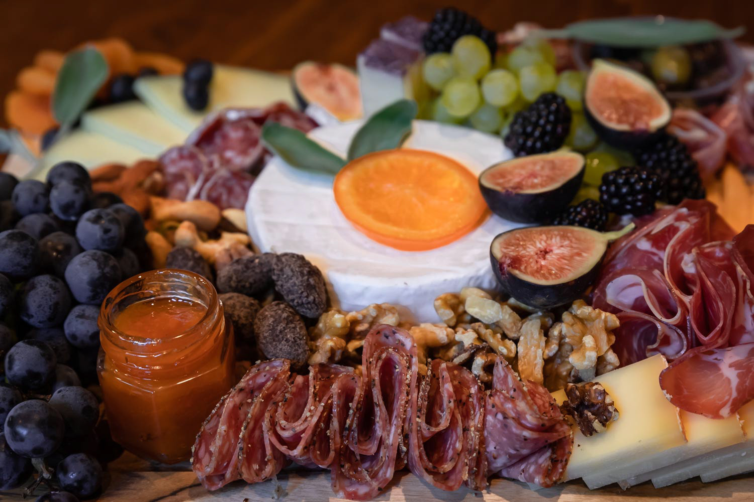 Food board with cured meats prosciutto, salami and coppa; brie, cheddar and other cheeses and fruits decorated with sage