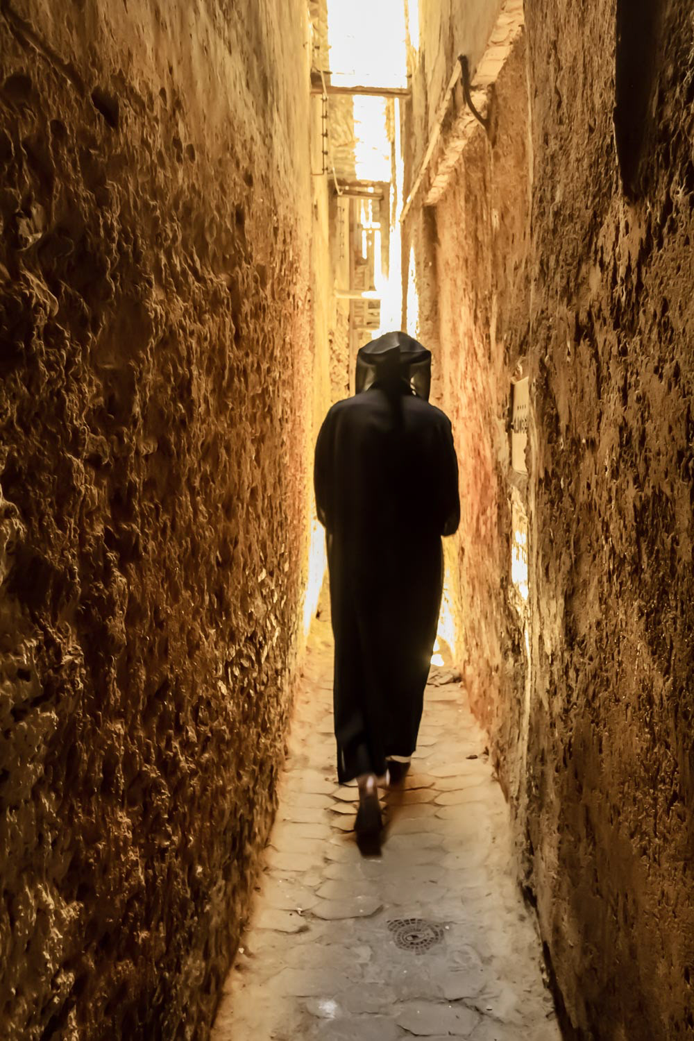 Unidentifiable man in a djellaba, berber clothing walking down a narrow street in Fes Medina in Morocco