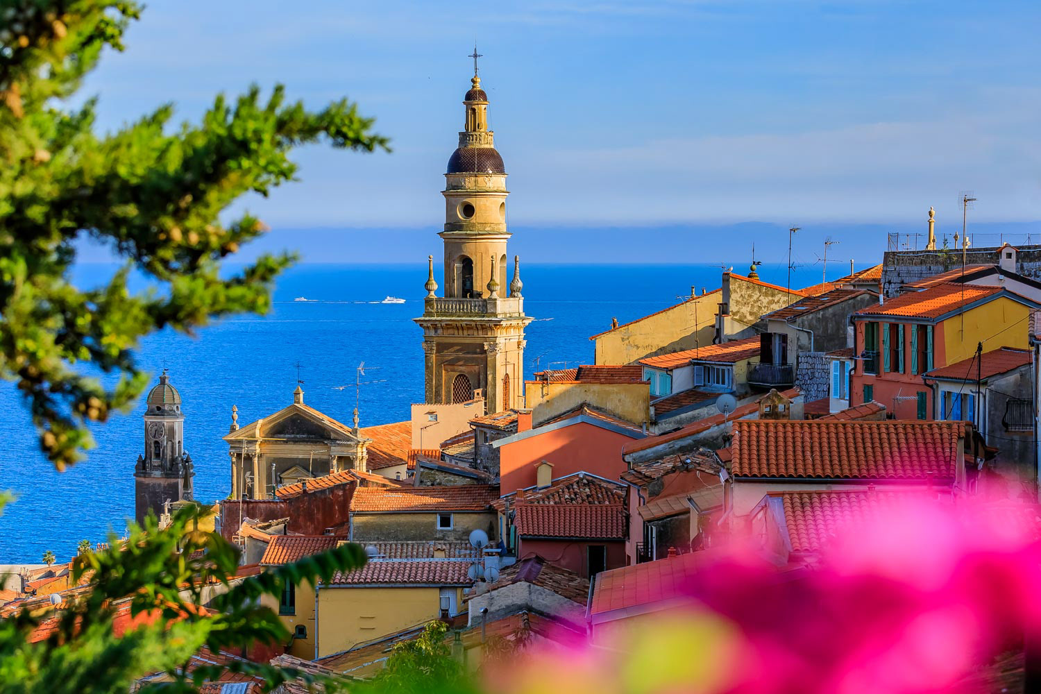 Church bell tower in Menton on French Riviera or Cote d'Azur with Mediterranean Sea in seen through green trees