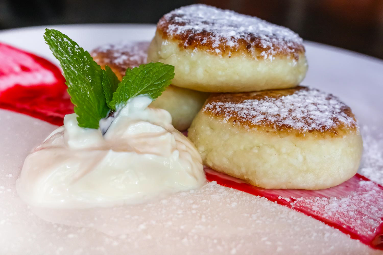 Traditional Russian sweet fried cheese cakes elegantly served on a plate with sour cream, jam and a mint leaf, sprinkled with powdered sugar in Taganrog, Russia
