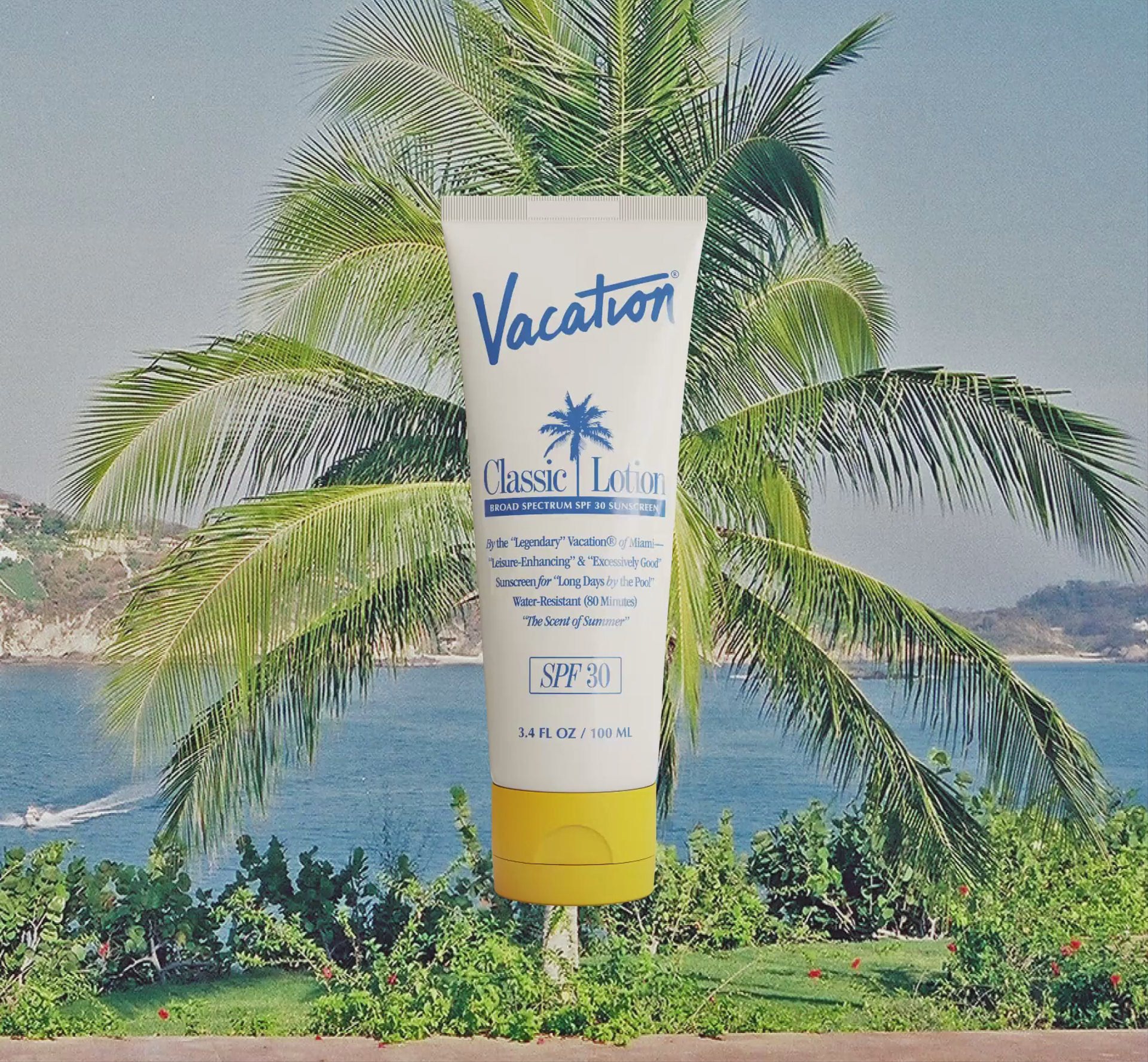 A tube of Vacation's Classic Lotion against a faded film photo of a palm tree with the ocean and mountains behind it.