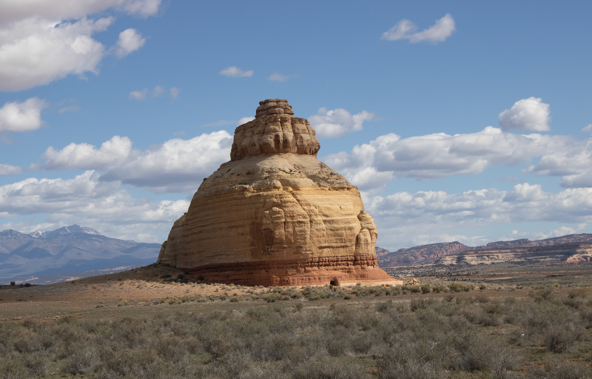 Towering layered sandstone butte rising from the high desert landscape beneath drifting cumulus clouds, showcasing dramatic geological formations of the American Southwest.