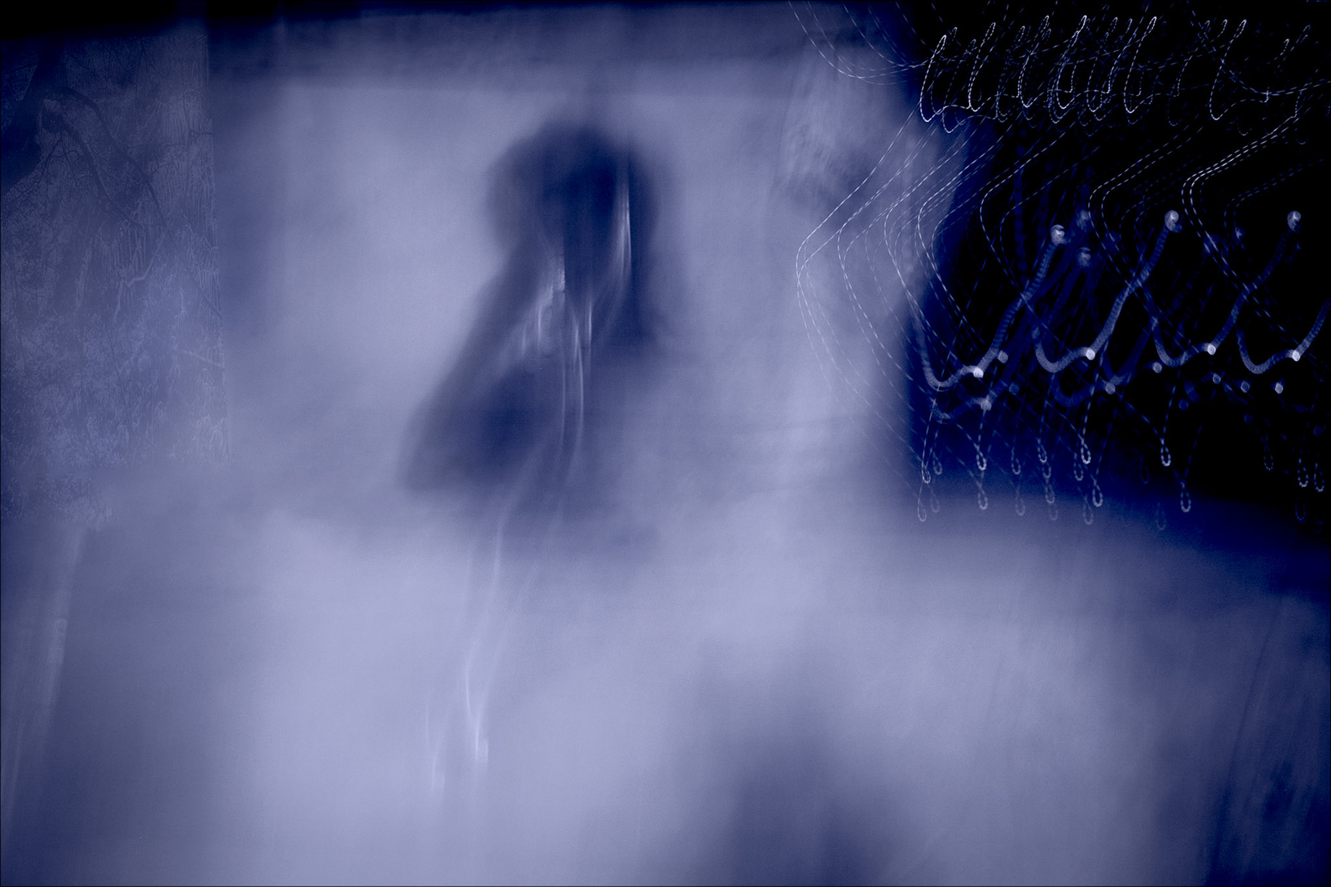 A surreal, abstract image dominated by dark blue and purple hues. In the center, a shadowy, indistinct figure blends into a misty background. On the right, intricate light patterns resembling delicate, floating threads add depth and complexity to the composition. The atmosphere is mysterious and dreamlike, evoking a sense of otherworldliness.