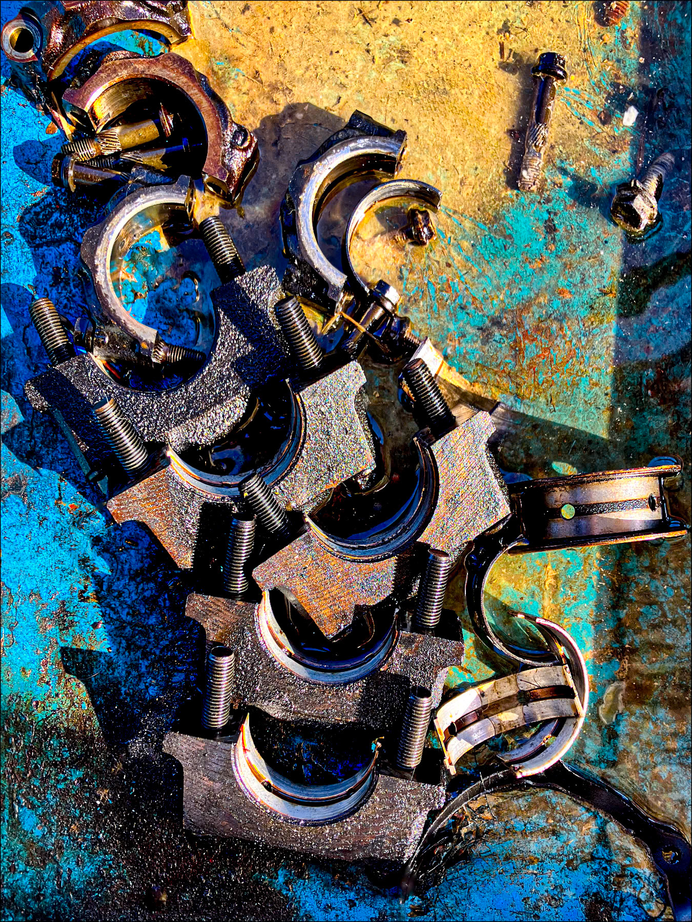 Dismantled mechanical crankshaft parts scattered on a worn surface, highlighted by oil reflections.
