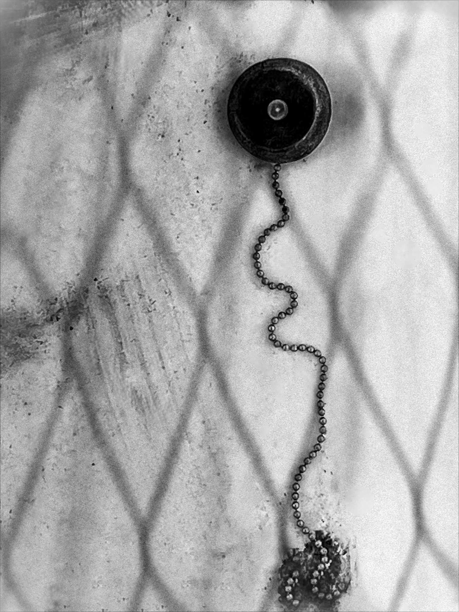 Black and white photograph. Black circular element with long hanging chain, suspended in absolute white suggesting total silence. Title: 1/500.000.000 | ©2025