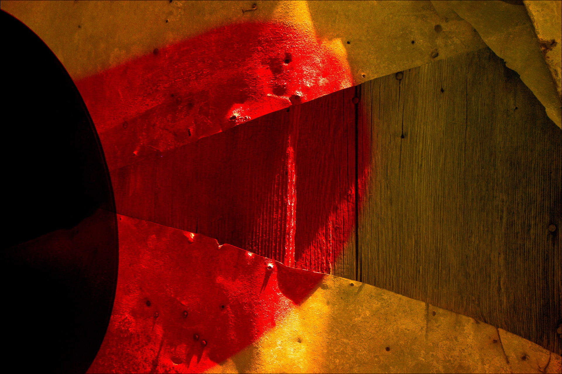 Abstract composition of metal and wood with red and yellow lights, shadow play and contrasting surfaces.