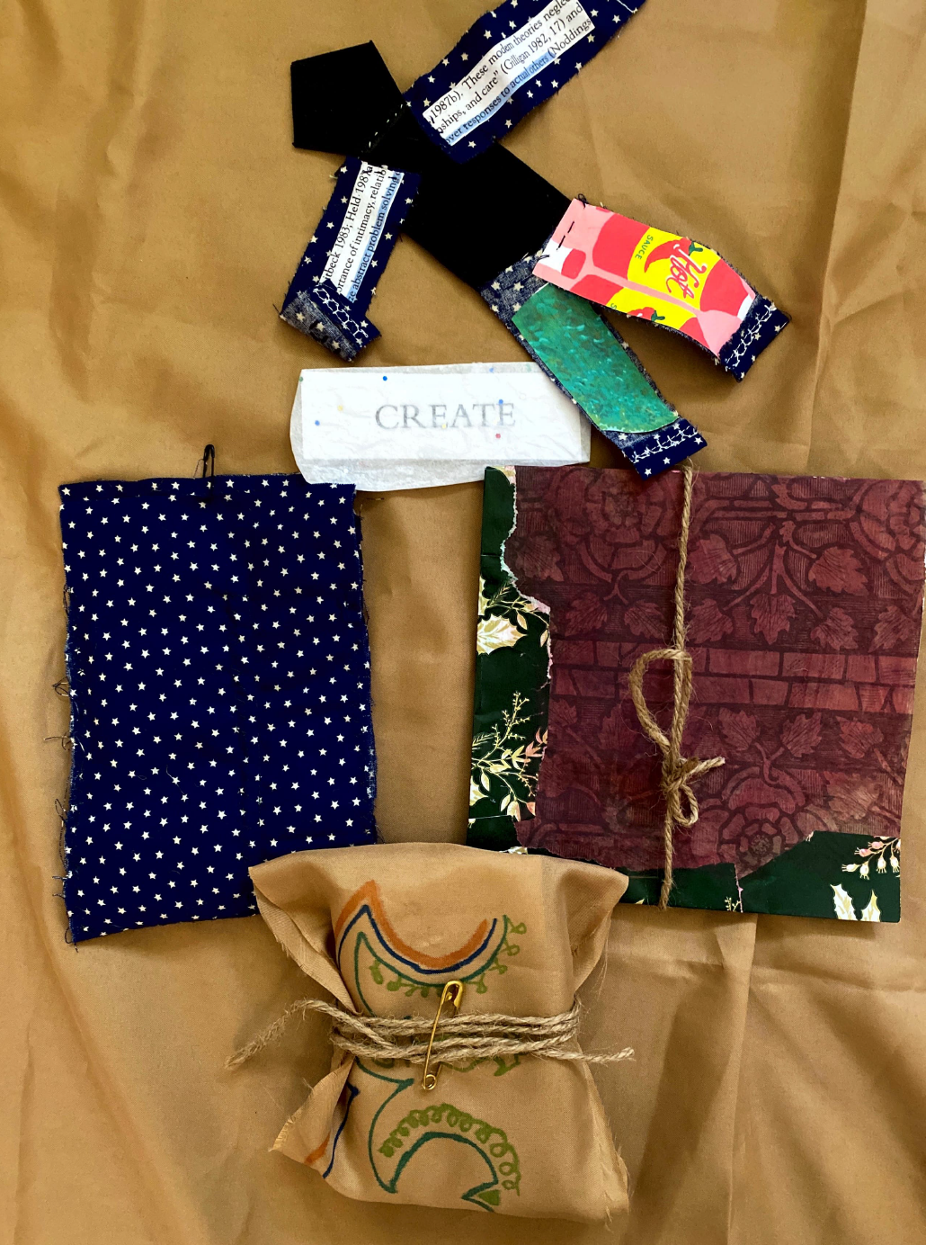 A paper doll and three packages are placed over a brown fabric.