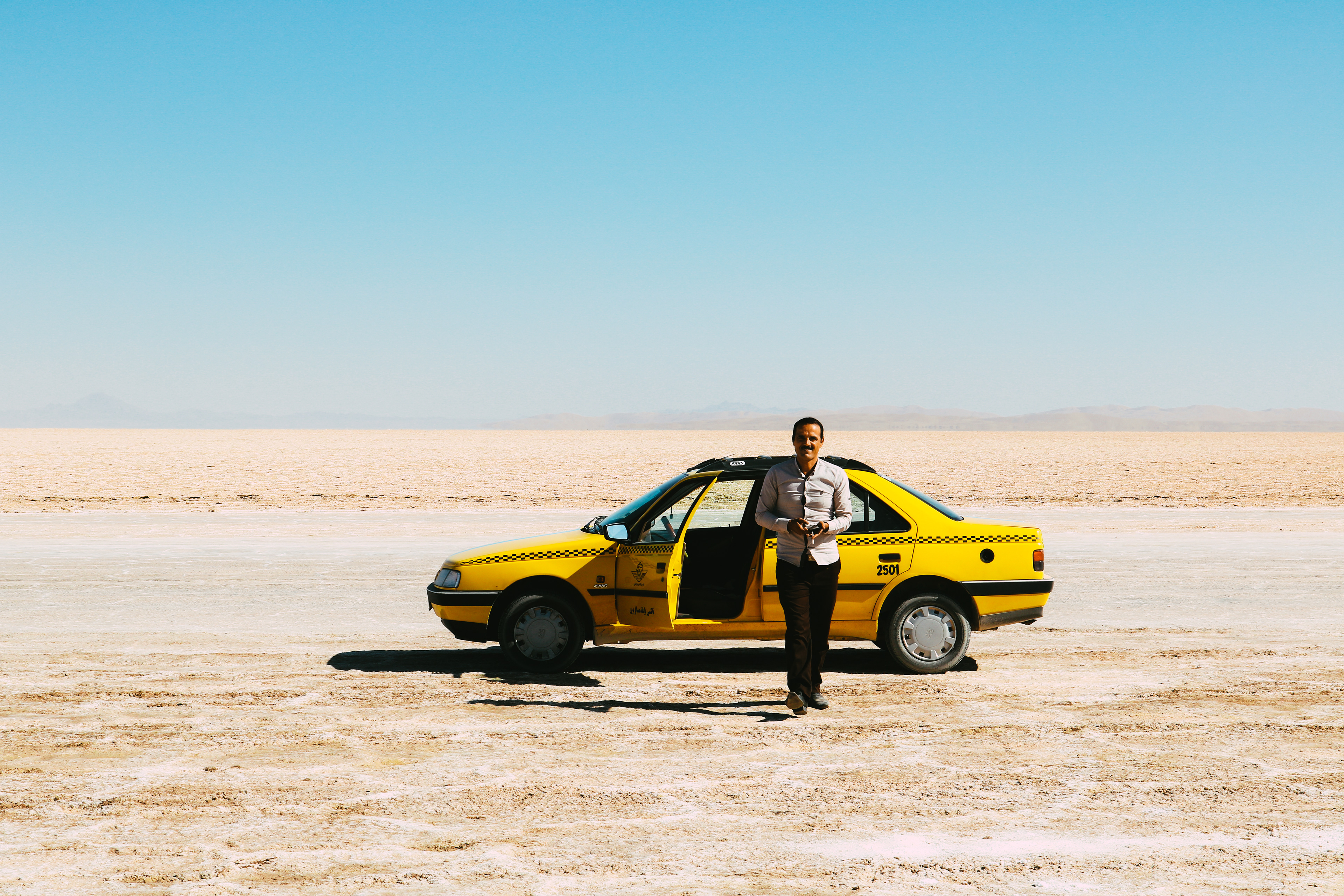 Iran, Kavir National Park. Taxi driver taking a cigarette break in the middle of the desert.