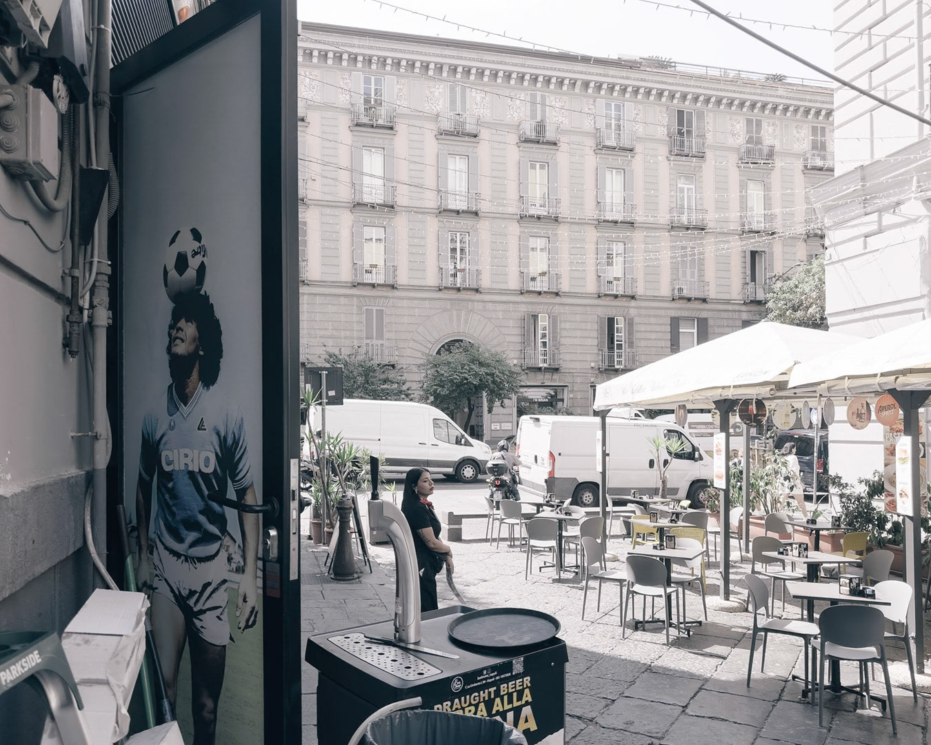Napoli, Italy - May 28, 2026: View from a café or bar entrance on Corso Umberto I, with outdoor tables, delivery vans, historic buildings, and a large Diego Maradona poster, reflecting the strong football culture visible throughout Naples