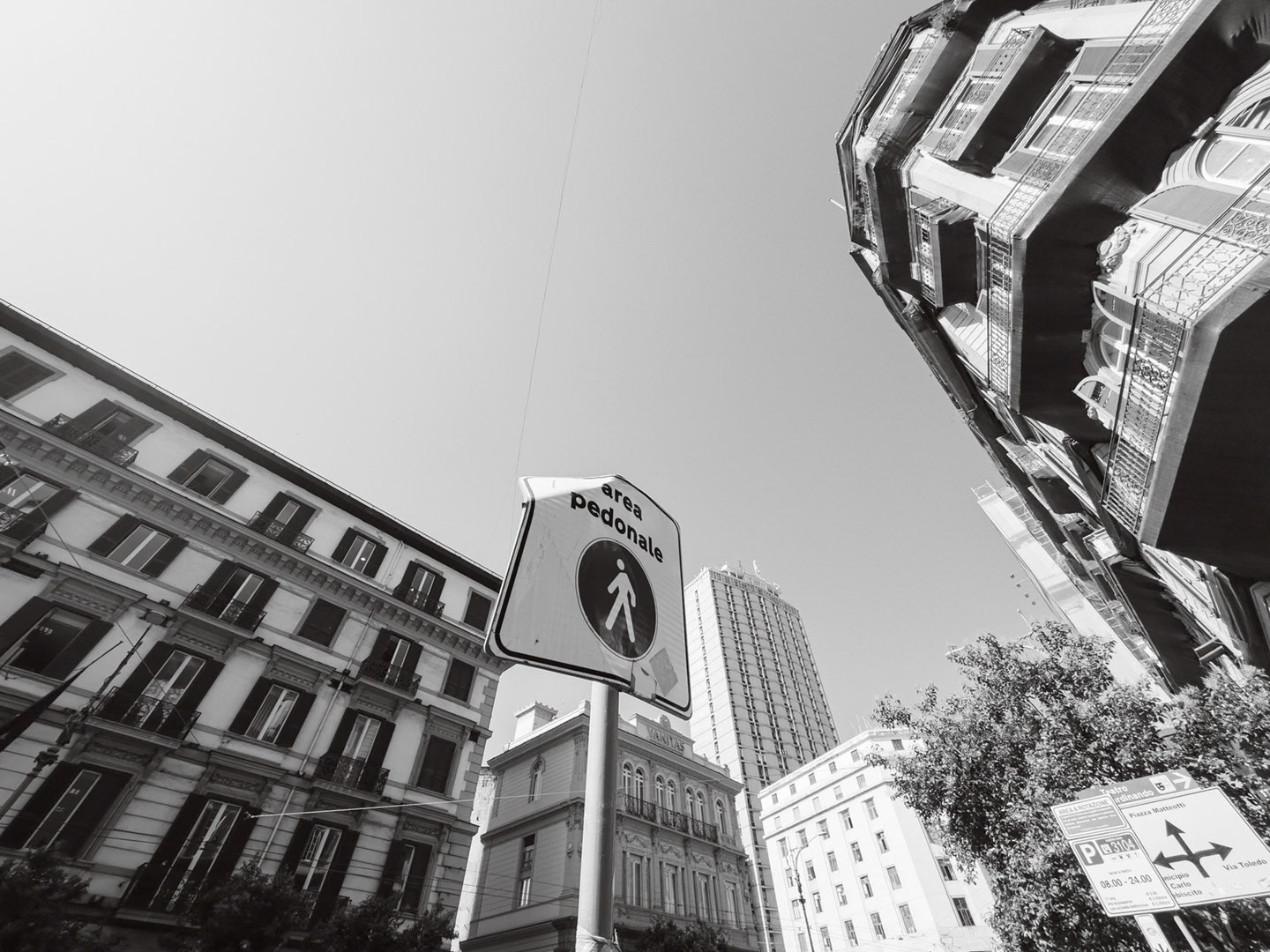 Napoli, Italy - May 27, 2026: Black and white low-angle view of a pedestrian area sign on Via Armando Diaz, surrounded by historic buildings, balconies, street signs, and modern high-rise architecture in central Naples