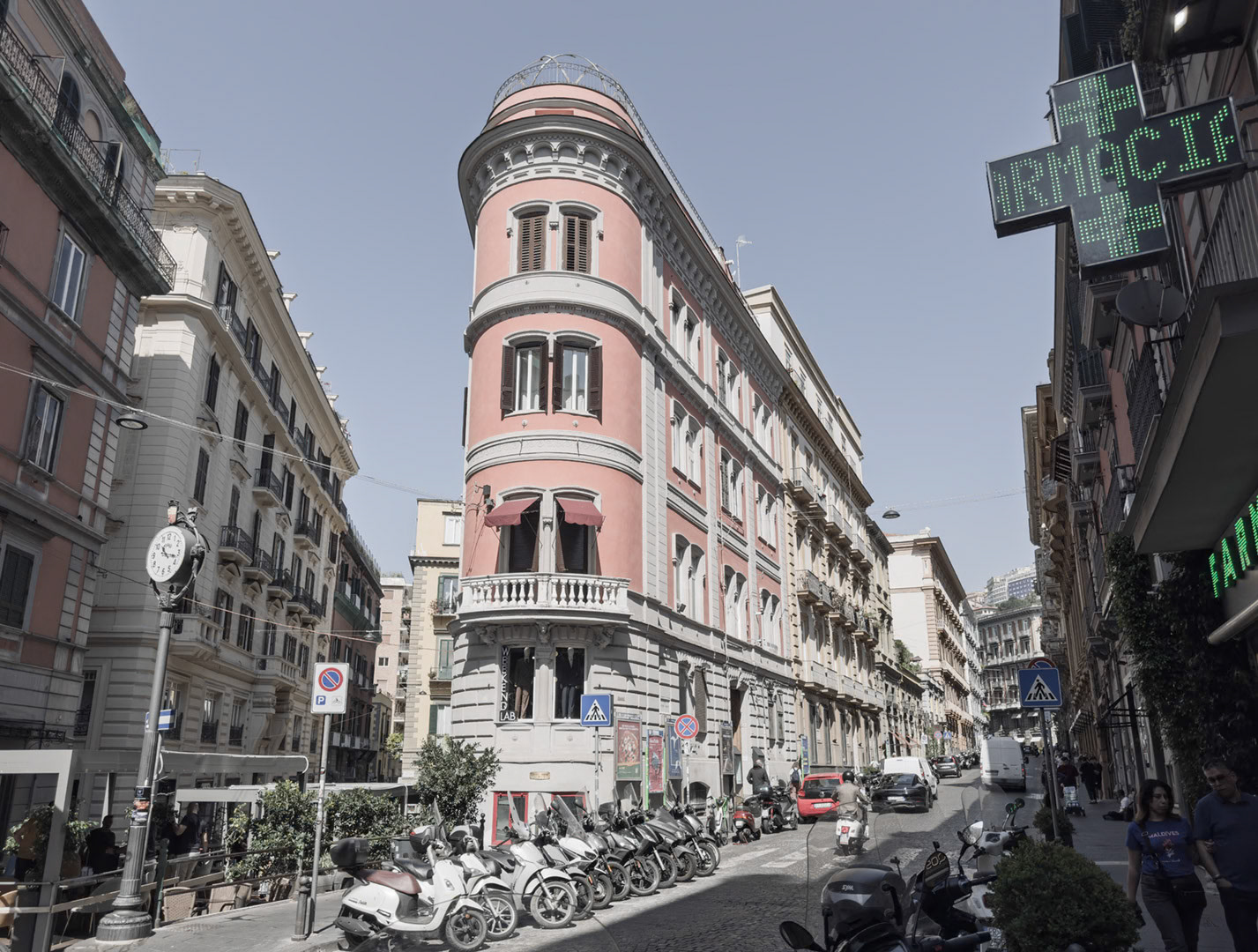 Napoli, Italy - May 27, 2026: View along Via Gaetano Filangieri in the Chiaia district, with elegant historic buildings, a pink corner facade, parked scooters, pedestrians, street signs, a pharmacy cross, and dense urban traffic in central Naples