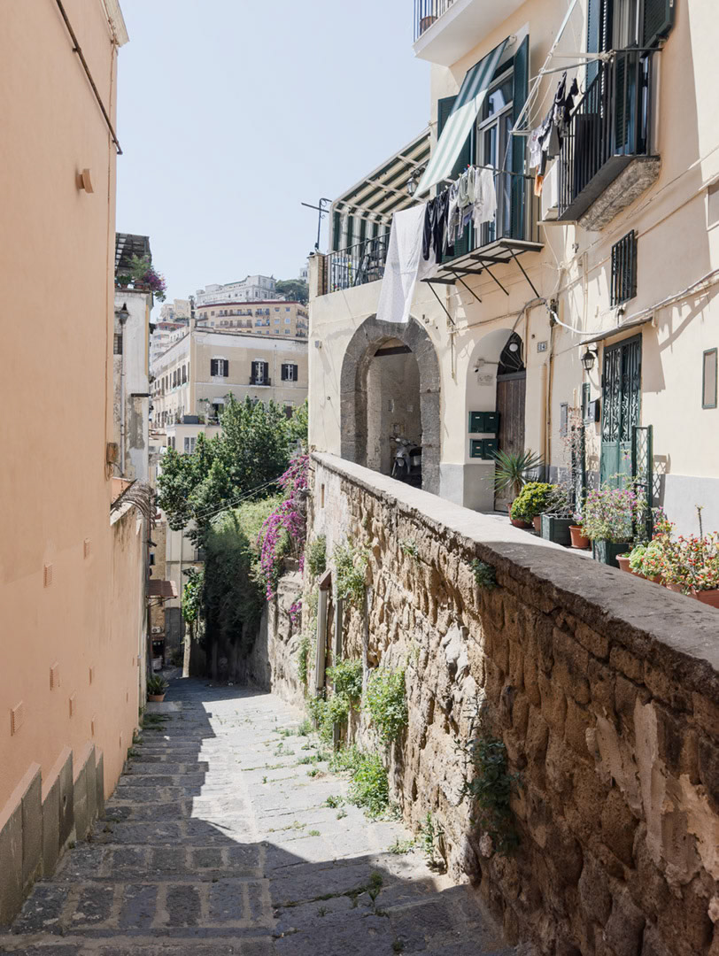 Napoli, Italia - May 27, 2026: View along the Scalinata della discesa del Petraio, a historic stepped street in Naples, with laundry hanging from balconies, potted plants, stone walls, residential buildings, and the city (Vomero) rising in the background.