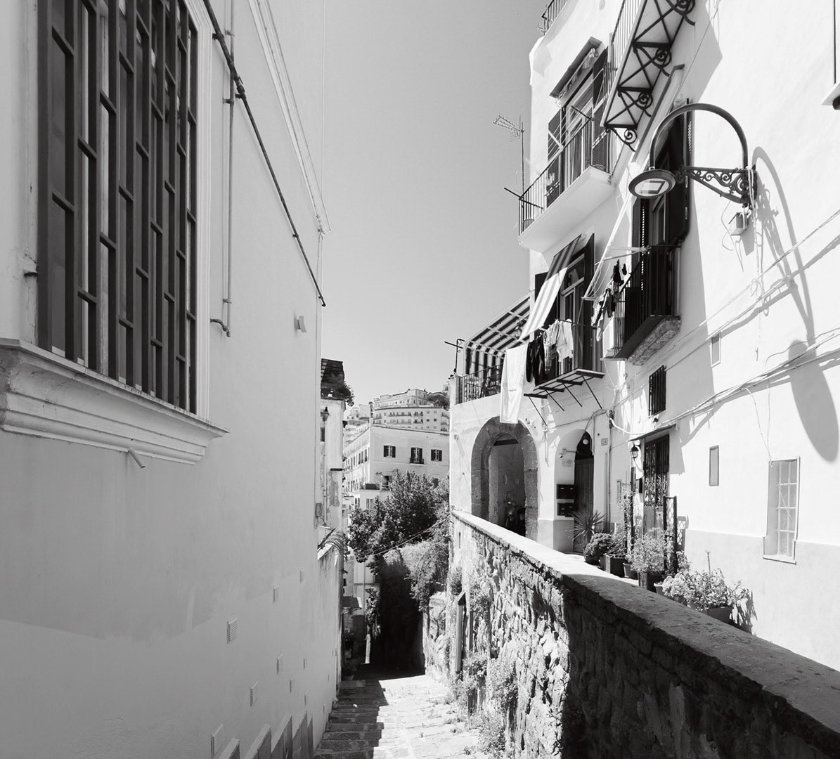 Napoli, Italy - May 27, 2026: Black and white view along the Scalinata della discesa del Petraio, with stone steps descending between residential buildings, balconies, hanging laundry, potted plants, wall shadows, and the Vomero district visible in the distant background.
