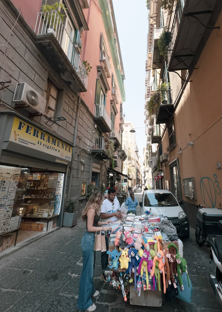 Napoli, Italy - May 27, 2026: Street vendor selling toys and small goods on Via Cavallerizza a Chiaia, a narrow street in Naples with pedestrians, parked cars, balconies, apartment buildings, shopfronts, and a hardware store sign