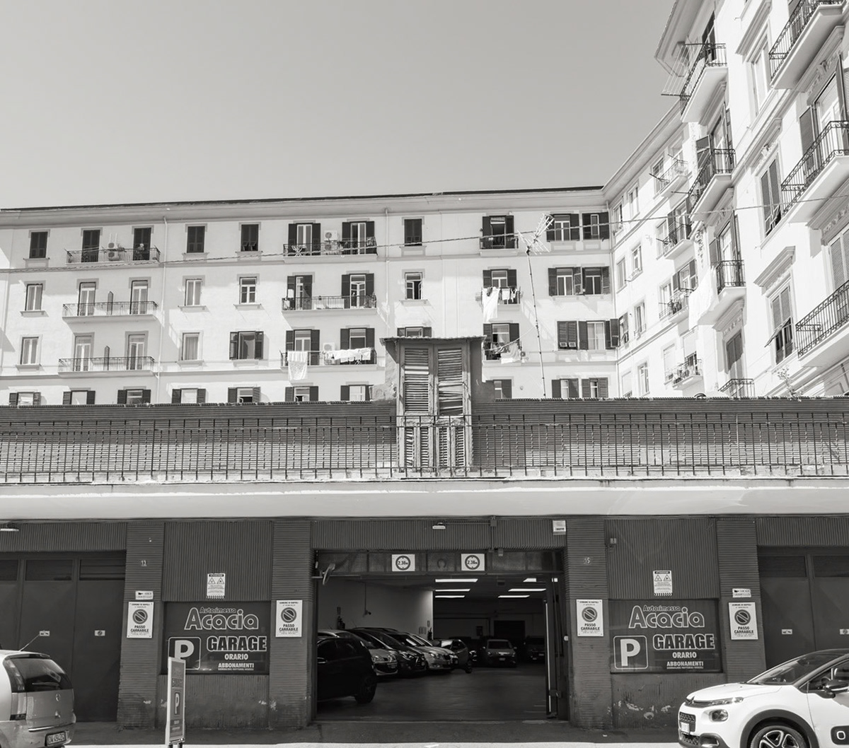 Napoli, Italy - May 27, 2026: Underground parking garage on Via Renato Lordi below dense residential apartment buildings, with balconies, laundry, parked cars, and signs advertising hourly parking and subscriptions in a city where parking spaces are valuable.