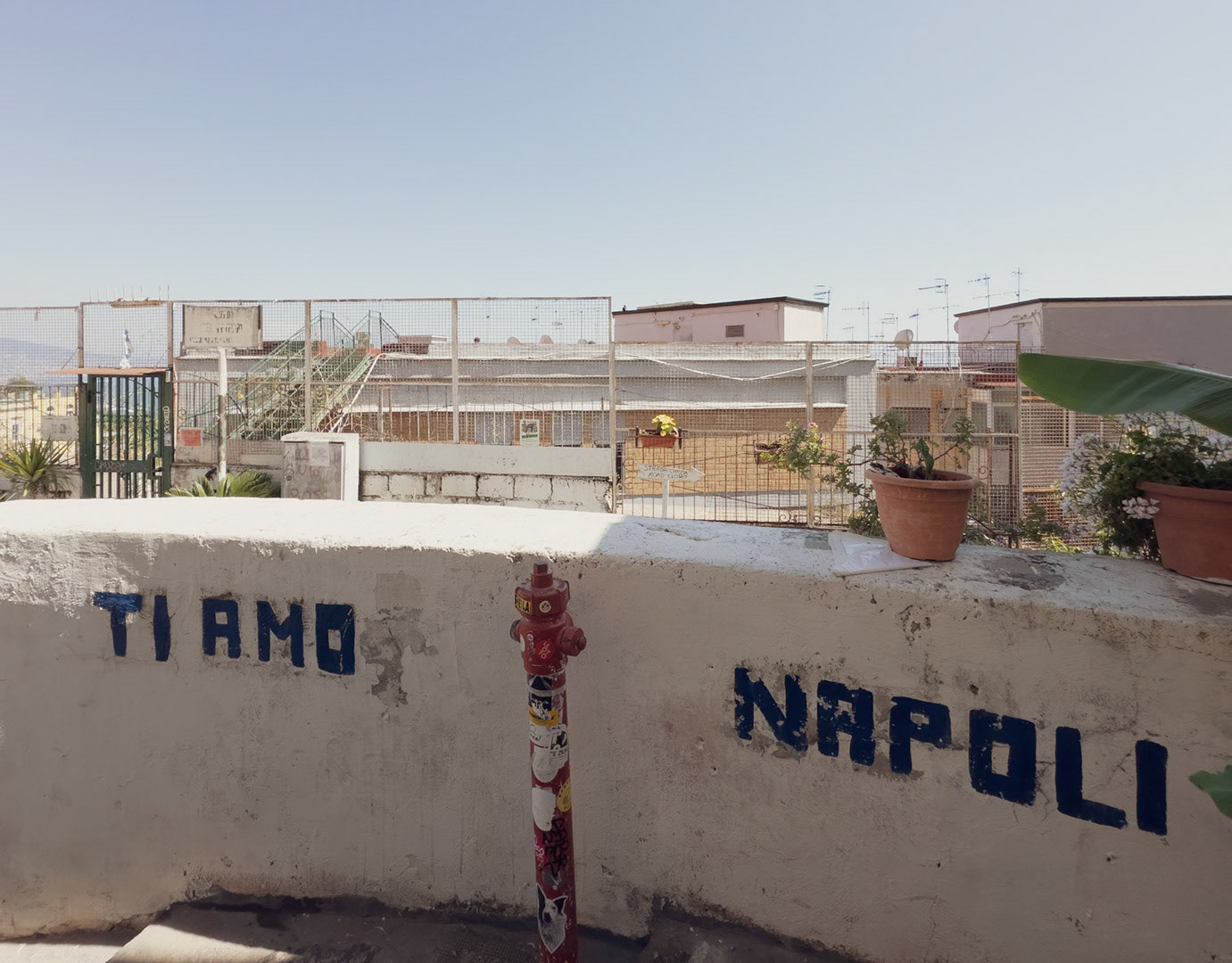 Napoli, Italy - May 27, 2026: Urban view from near the top of the Scalinata della discesa del Petraio, with “Ti amo Napoli” graffiti painted on a low wall, a red fire hydrant, potted plants, rooftop terraces, metal fences, antennas, and the Gulf of Naples faintly visible in the distance