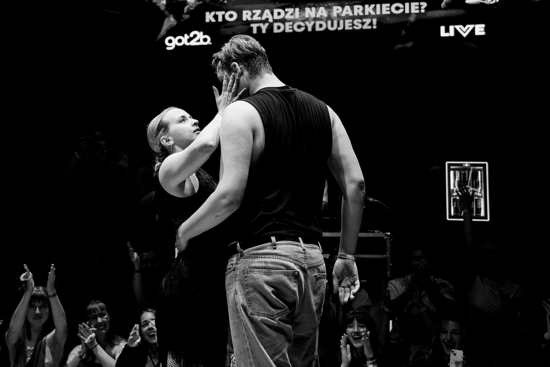 Dwójka tancerzy podczas Red Bull Dance Your Style w Poznaniu. Tancerka dotyka tancerza po twarzy. Zdjęcie jest czarno-białe.