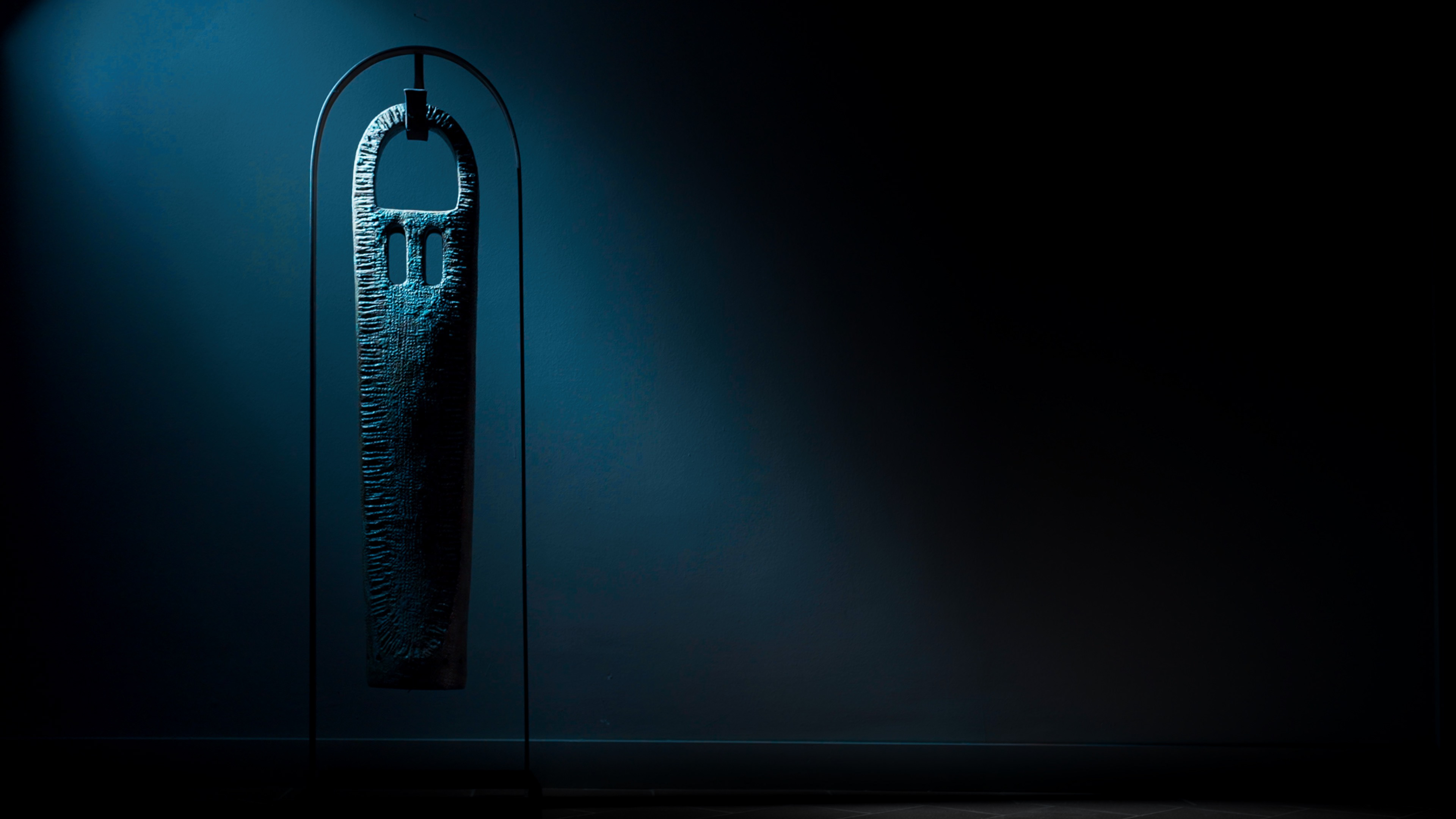 Scultura di Bruno Bagnoli di arte contemporanea illuminata su fondo scuro all'interno di uno spazio espositivo.