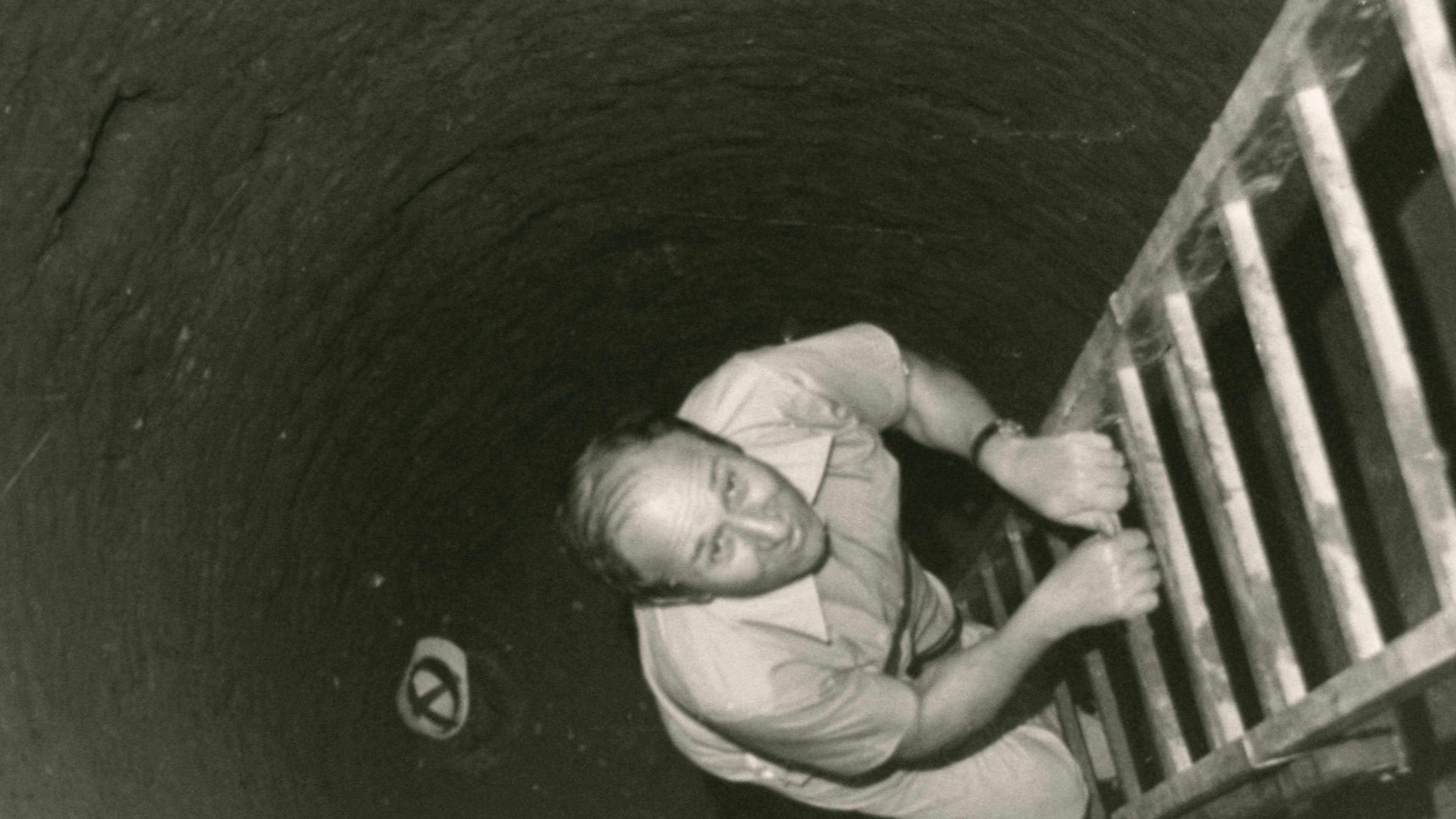 foto antica di un uomo che risale un pozzo con una scala a pioli