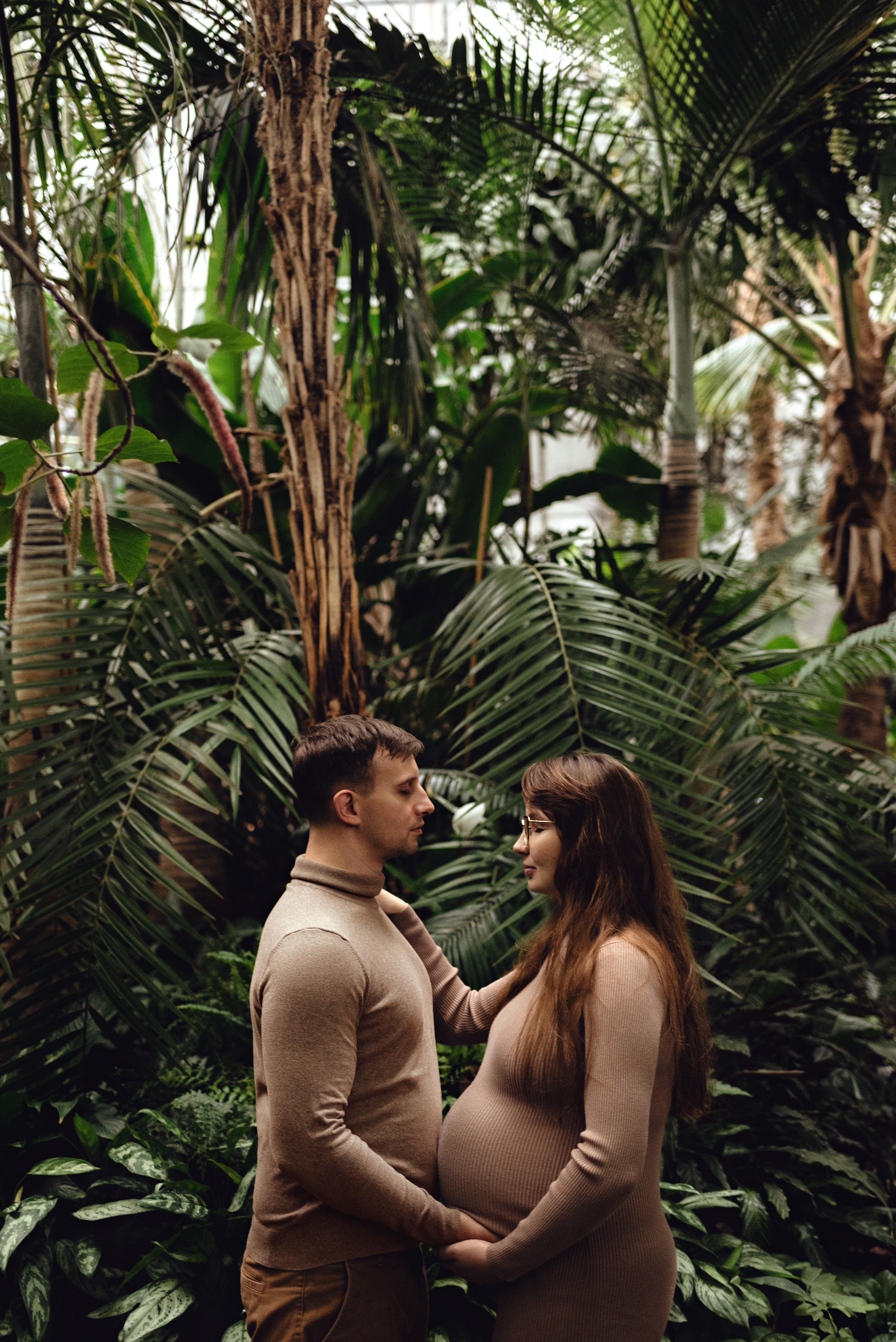 Sesja ciążowa w palmiarni w Gliwicach. Przyszli rodzicie na tle tropikalnych drzew, plam i roślin. Tata i mama w ciaży w trakcie sesji ciążowej w ogrodzie botanicznym. 