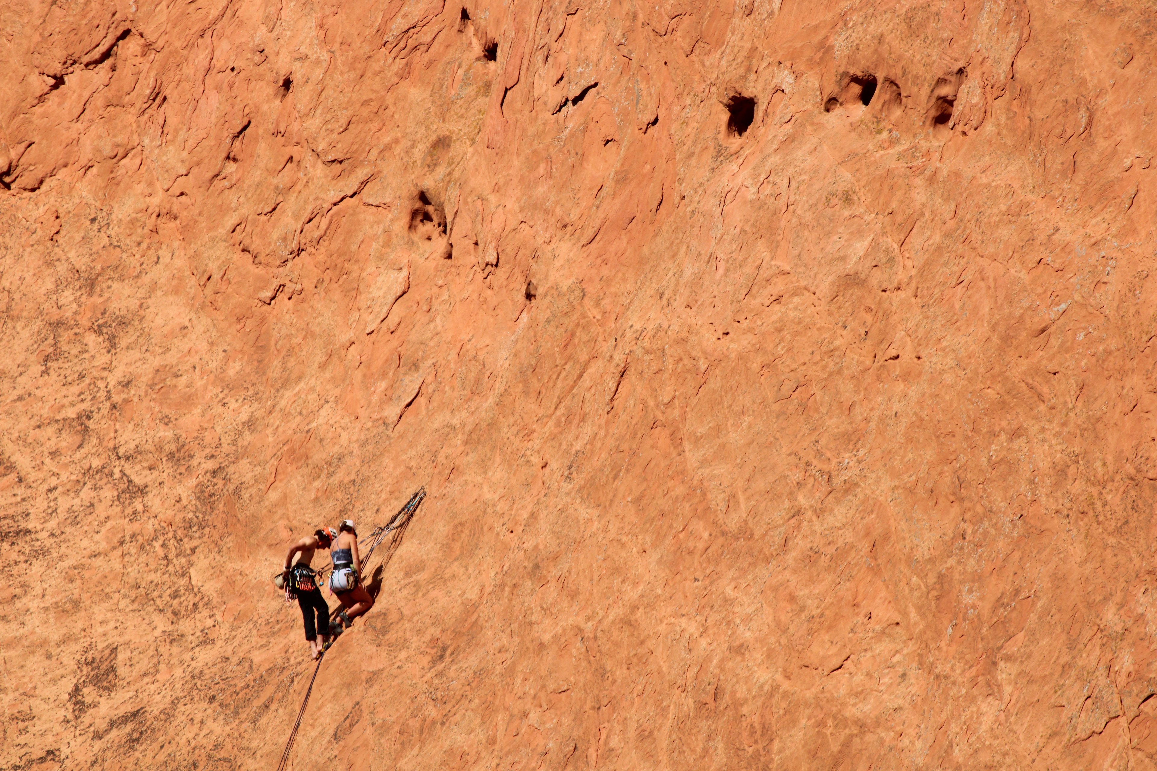 Two rock climber pause for a break while climbing in the Garden of the Gods in Colorado on October 5, 2024. The climber on the left just kicked her climbing shoes off the rock face, likely because climbing shoes can become painfully tight when not actively climbing. 
