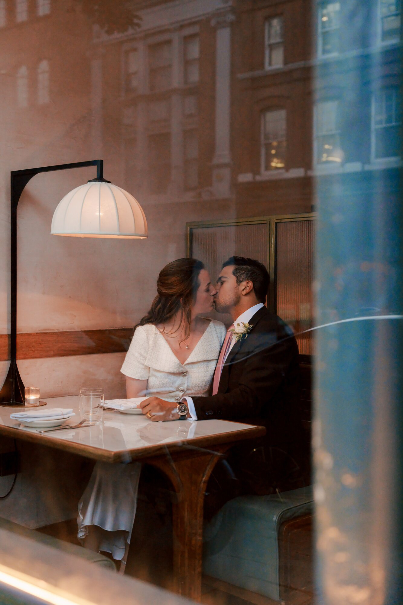 Window reflection portrait of the bride and groom kissing at Luca restaurant, London