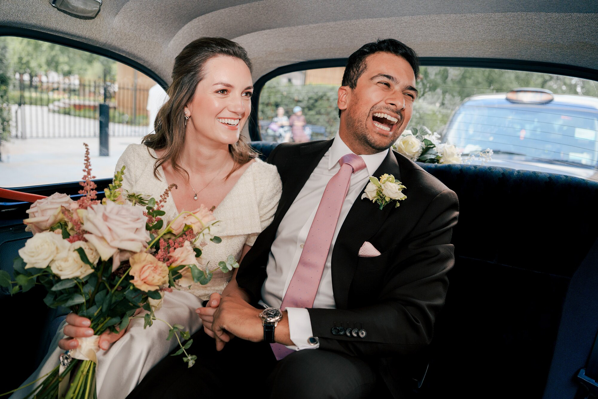 Bride and groom laughing in the back of a London black cab on the way to Marylebone Town Hall