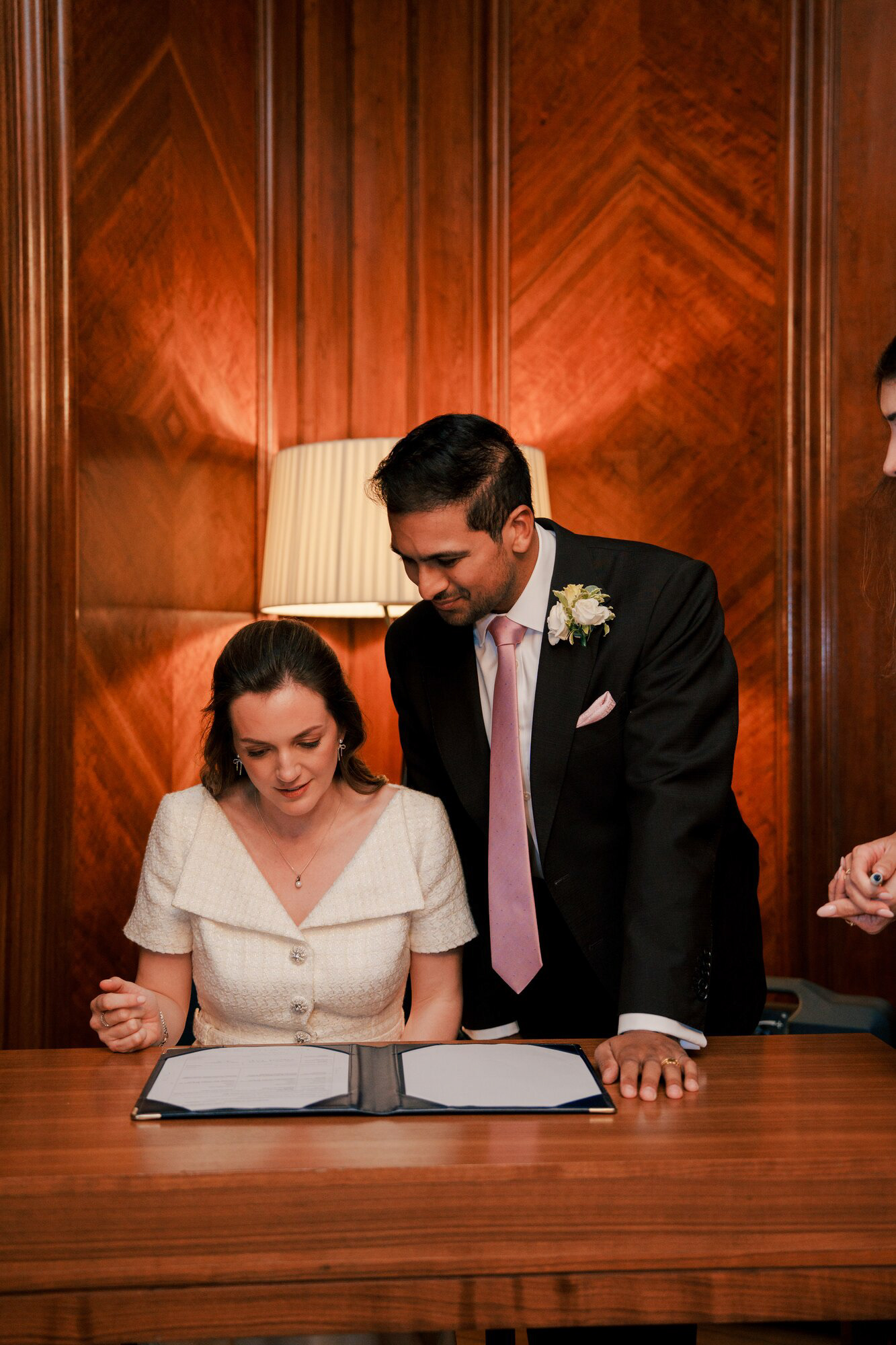 Bride signing the marriage register with the groom beside her at Marylebone Town Hall